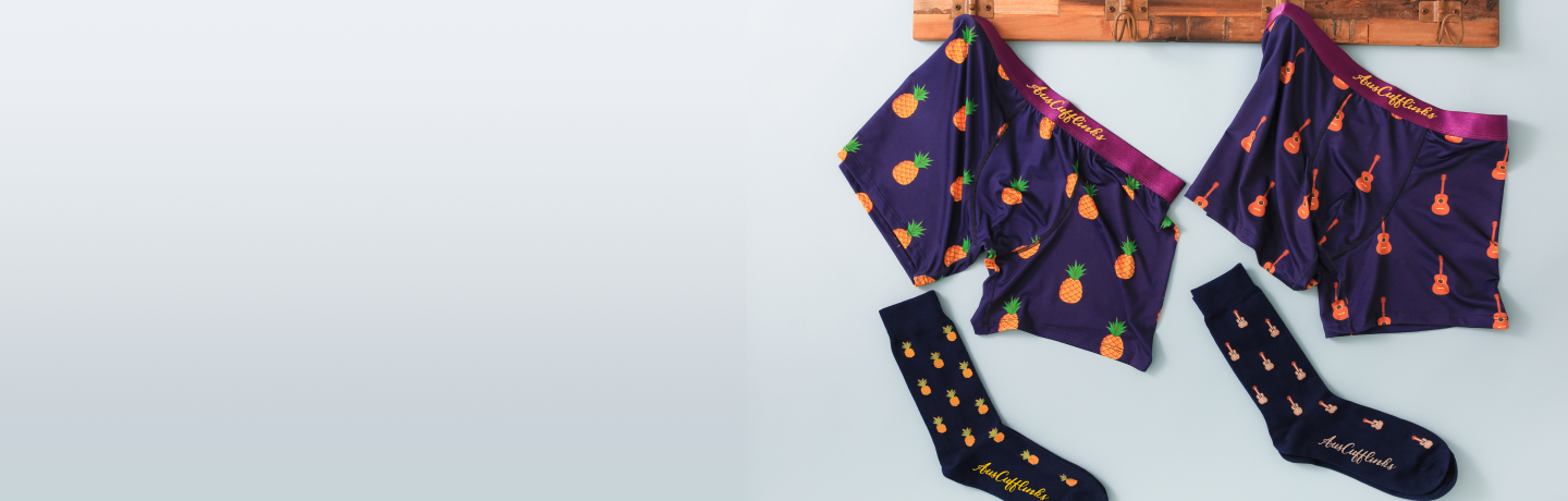 Matching purple boxer shorts and socks with pineapple design hung on a wooden hanger against a light background.