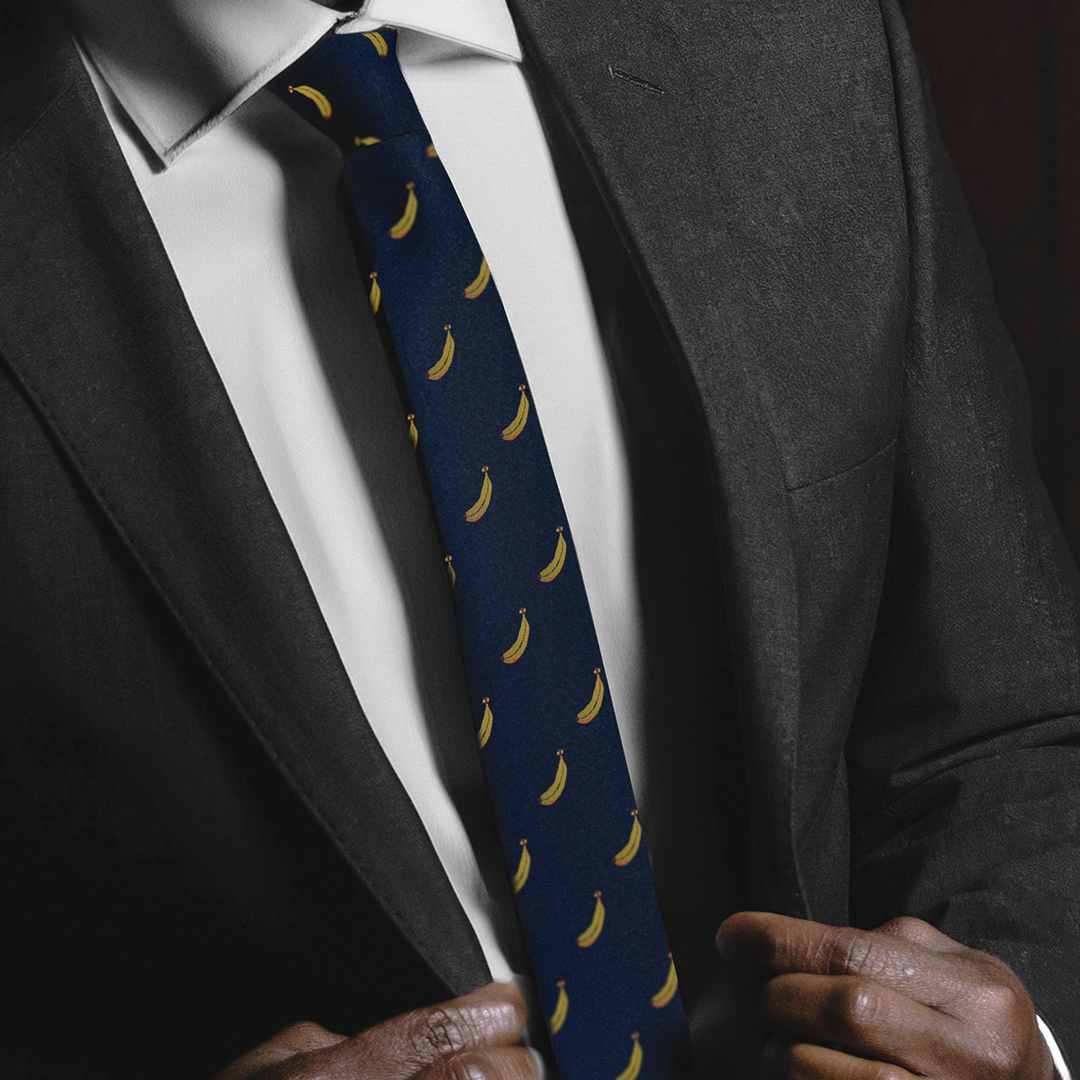 A person adjusts a dark suit jacket, revealing a white shirt and a Banana Thin Tie, embodying modern elegance.
