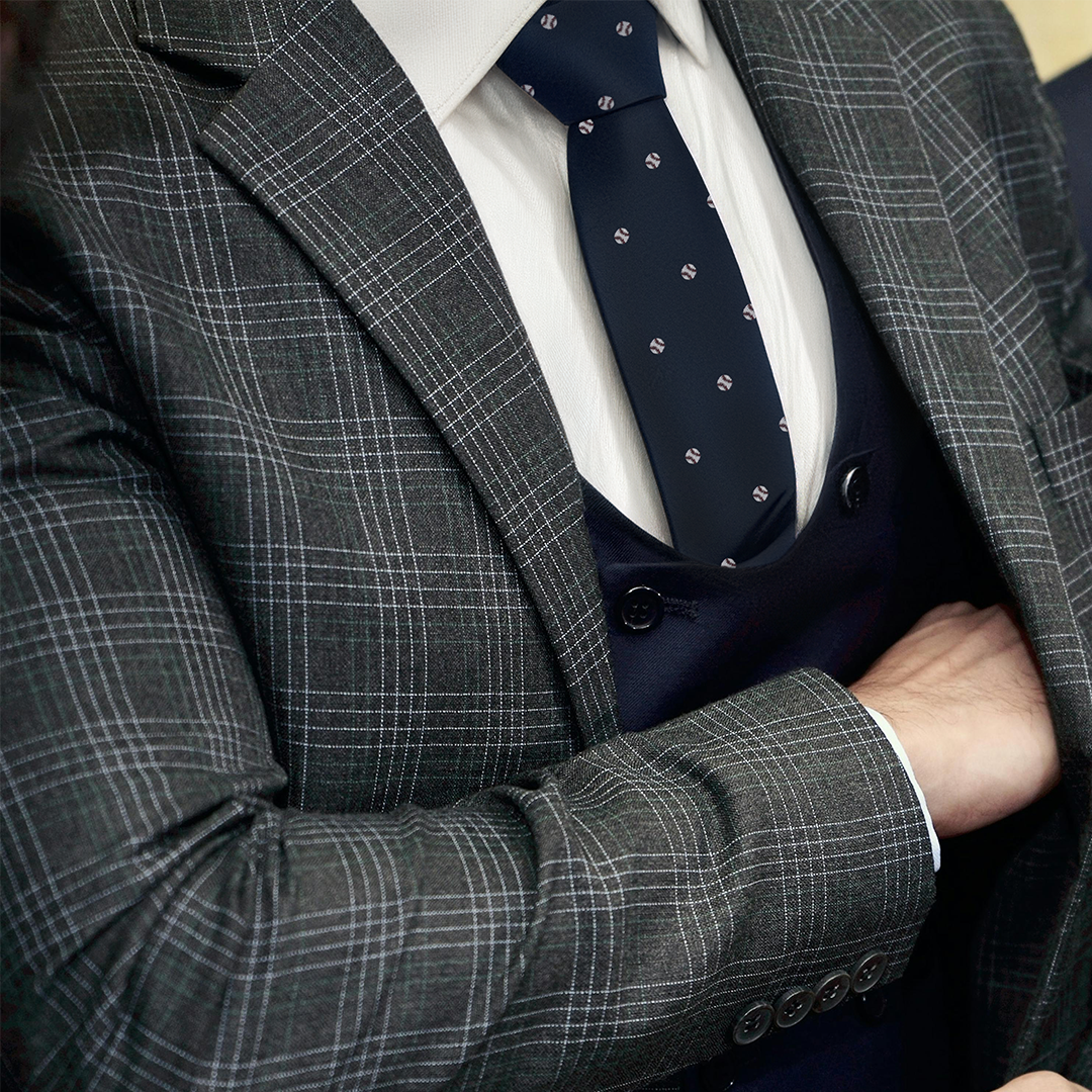 A person in a plaid suit and Baseball Slim Tie crosses their arms, exuding an air of elegance mixed with the confident poise of sportsmanship.