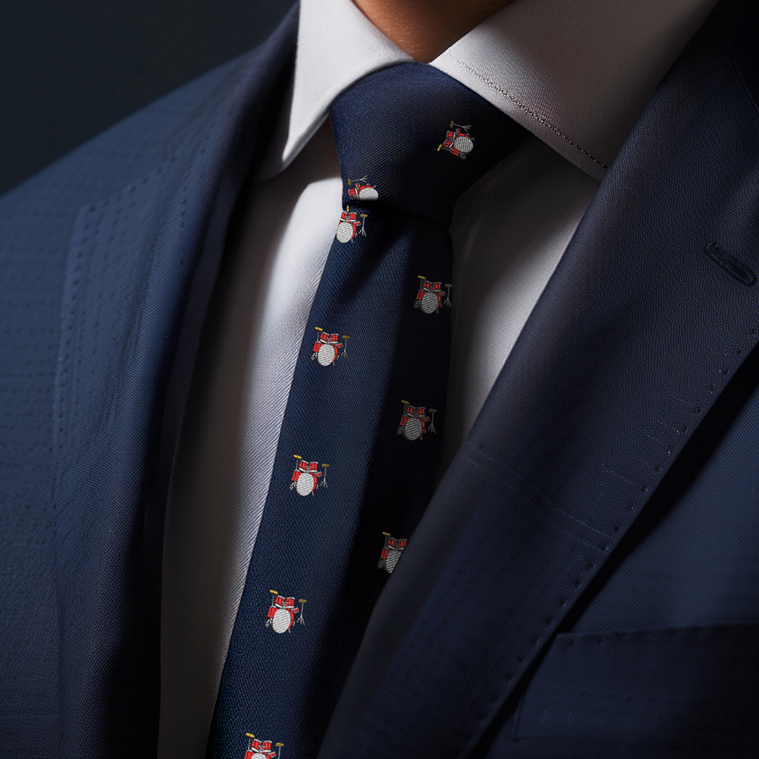 A person in a dark blue suit and a white shirt wears a Drums Thin Tie adorned with small drum set patterns, capturing a captivating style that's perfectly in tune with the beat of drums.