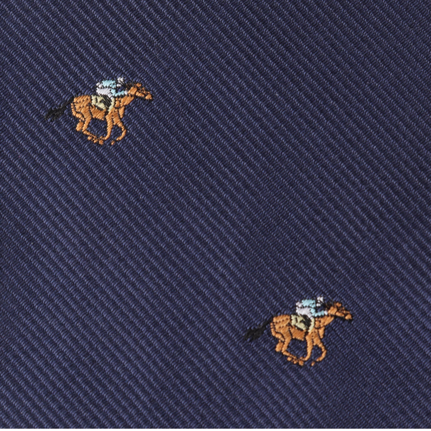 The Horse Racing Skinny Tie features navy blue fabric with small, embroidered brown horses and jockeys in blue shirts, arranged in a diagonal pattern—perfect for anyone who loves elegant equestrian style.