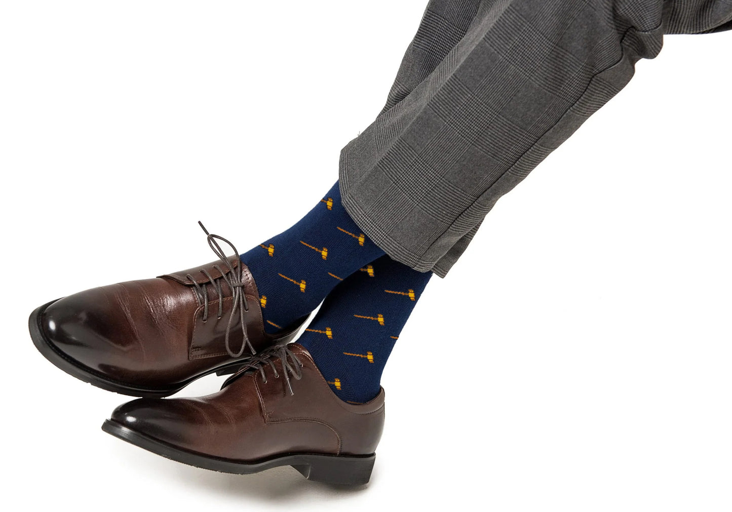A person wearing gray plaid trousers, brown leather dress shoes, and Gavel Socks—navy blue legal-themed socks with a small yellow gavel pattern.