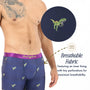 A man models T-Rex Underwear—blue boxers with a small green T-Rex print. An inset shows tiny fabric perforations, and text highlights the breathable, moisture-wicking material.