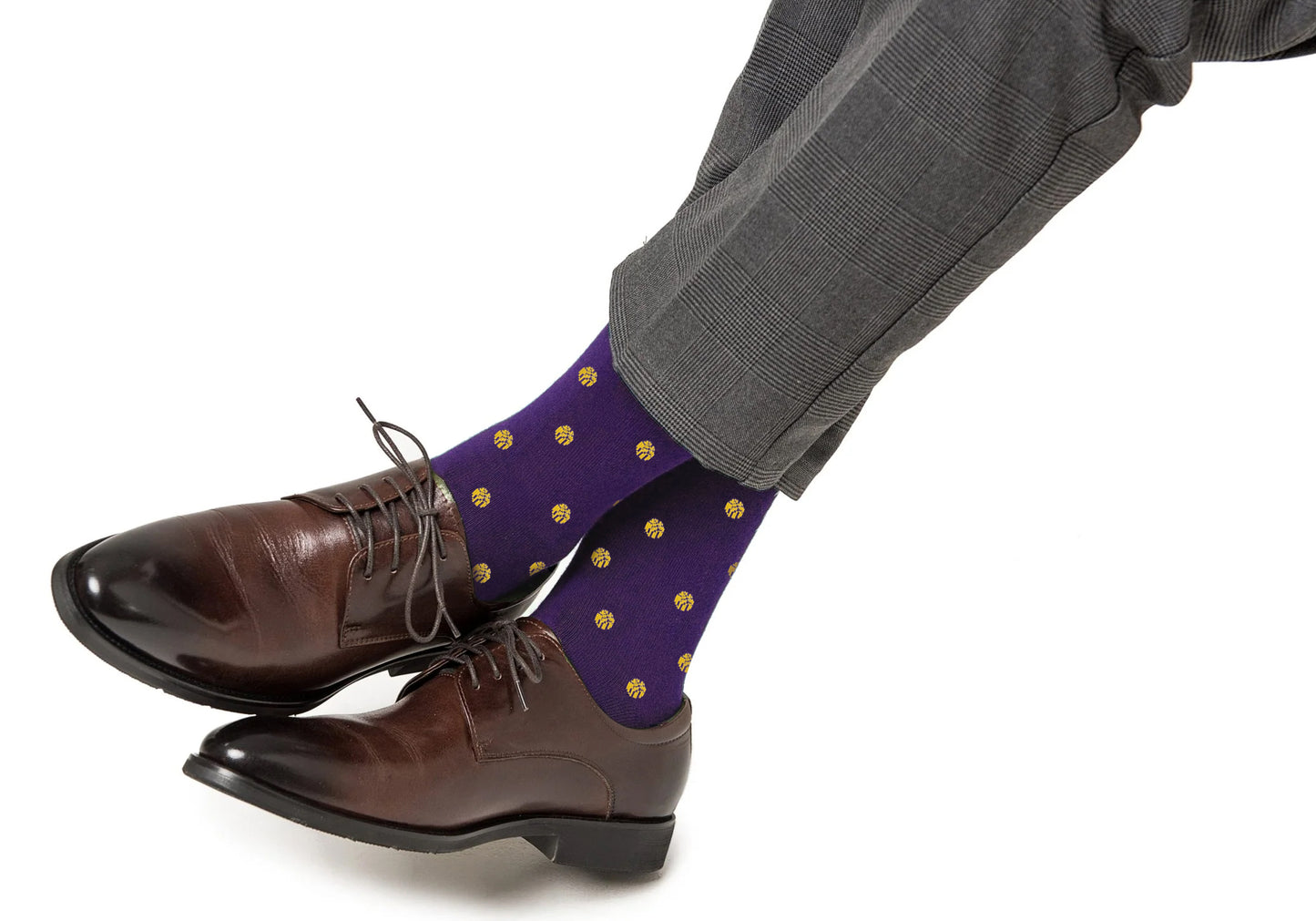A person sits with legs crossed, wearing brown dress shoes, gray plaid trousers, and Yellow Basketball Socks inspired by NBA colors.