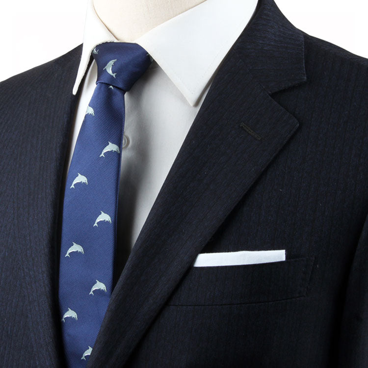 A person wearing a dark suit, white dress shirt, and a Dolphin Skinny Tie with a dolphin-inspired design featuring white dolphins, complemented by a white pocket square. Perfect for ocean enthusiasts.