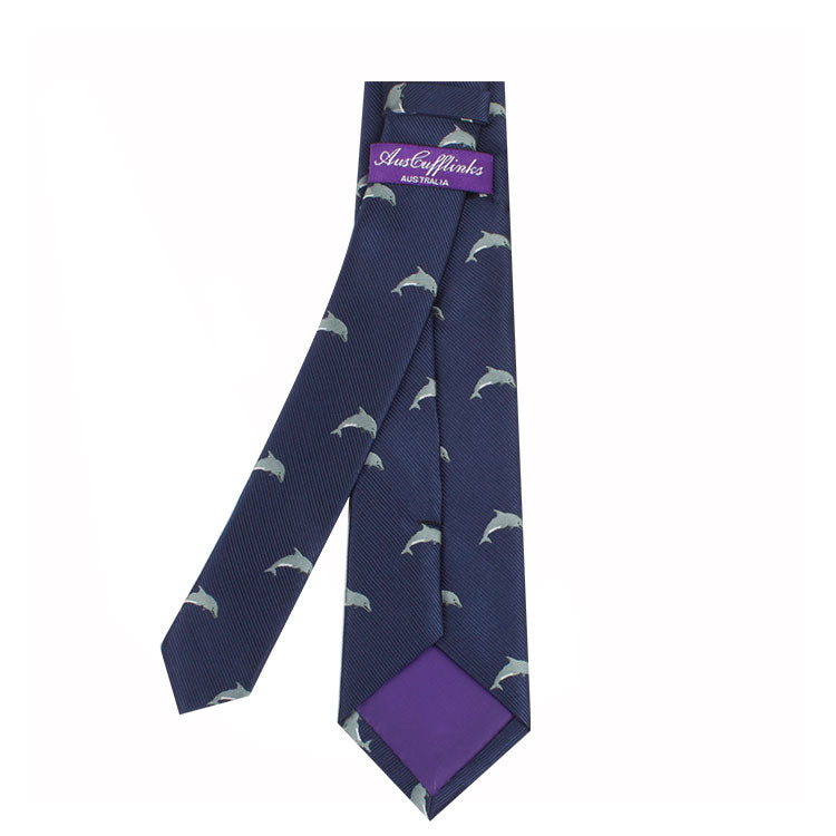 A navy blue Dolphin Skinny Tie with a dolphin-inspired pattern of silver dolphins, featuring a purple label on the back. Perfect for ocean enthusiasts.