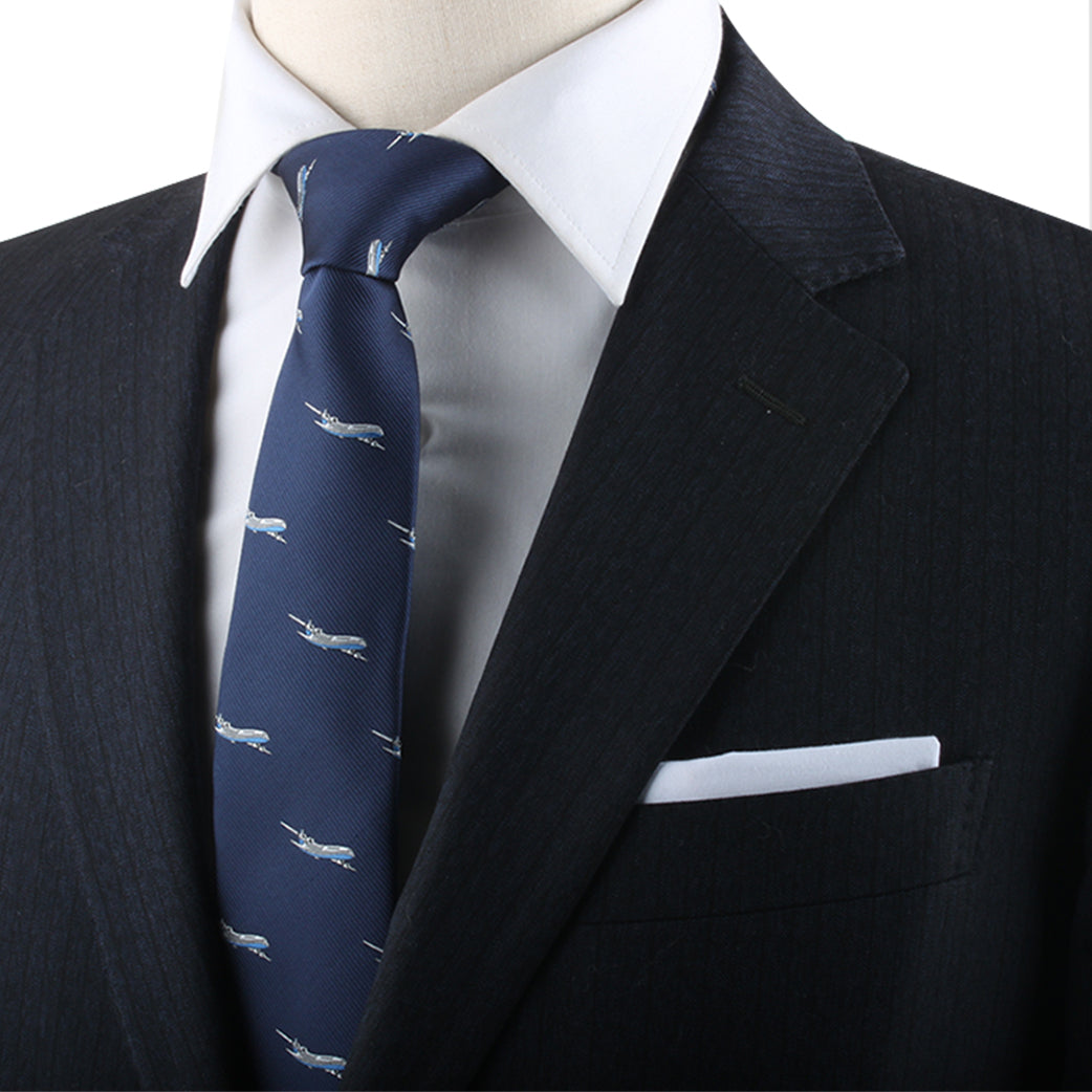 Close-up of a person wearing a black suit, white dress shirt, and an Air Travel Necktie adorned with white airplane patterns, exuding both aeronautical charm and style. A pristine white pocket square is neatly placed in the suit's breast pocket.