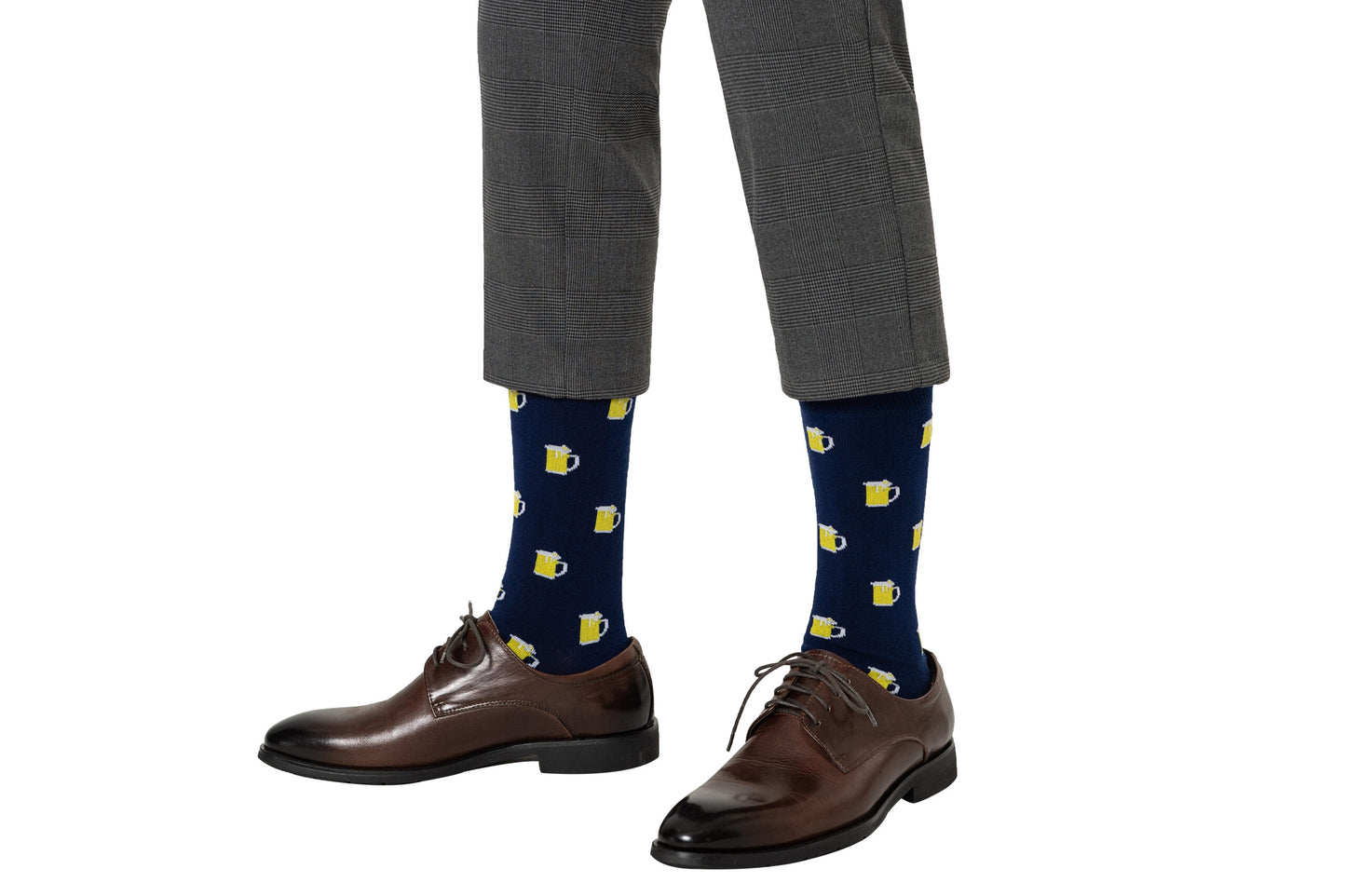 A person wears gray plaid trousers, brown leather dress shoes, and navy blue Beer Socks with yellow beer mug patterns—Beer Socks are fun socks perfect for beer lovers—shown on a white background.