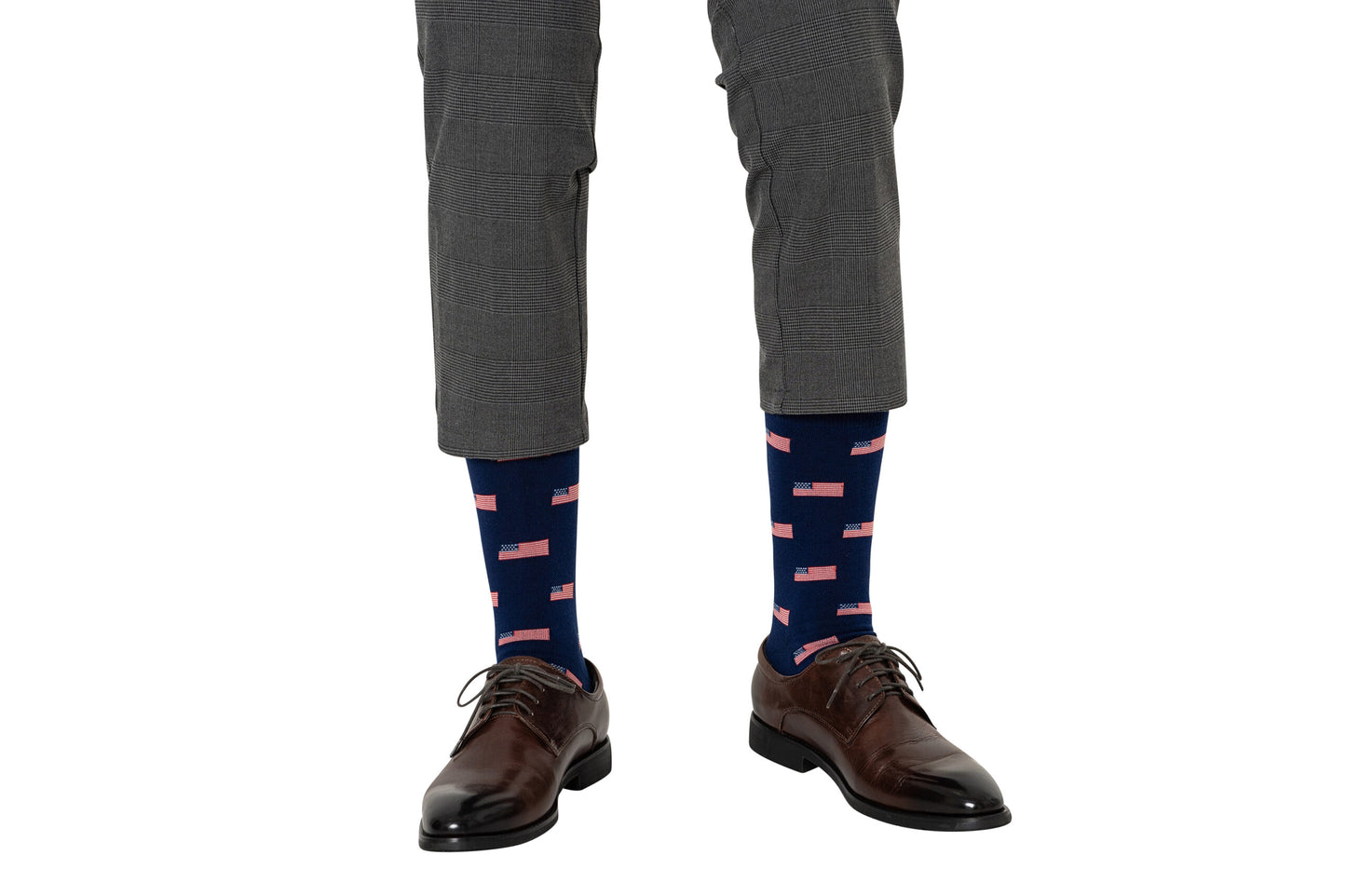 A man wearing gray plaid pants stylishly pairs brown dress shoes with USA Flag Socks, showcasing stars and stripes in blue and red.