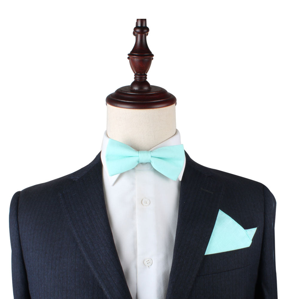 A black pinstriped suit along with a white shirt, light blue bow tie, and an Aqua Pocket Square is displayed on a mannequin, each fold crafted with finesse.