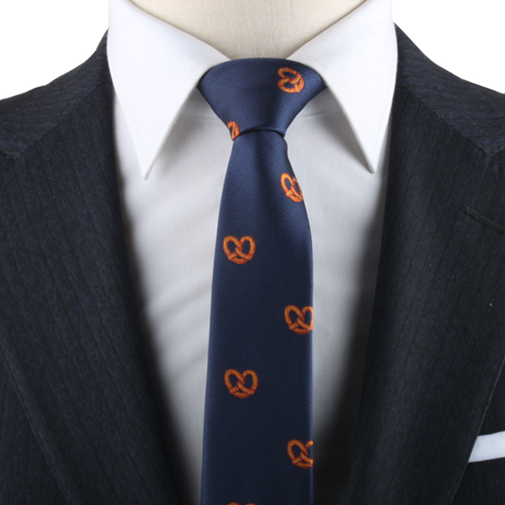 Close-up of a person wearing a dark suit, white shirt, and a navy blue Bagel Lover Tie adorned with small orange pretzel patterns, adding a touch of culinary delight to their contemporary style.