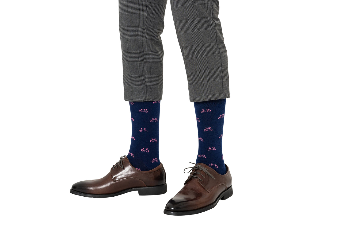 A man wearing gray checkered pants and dark brown shoes enjoys the comfort of his quirky choice of pink socks adorned with red bicycle patterns, pedaling through the day with style.