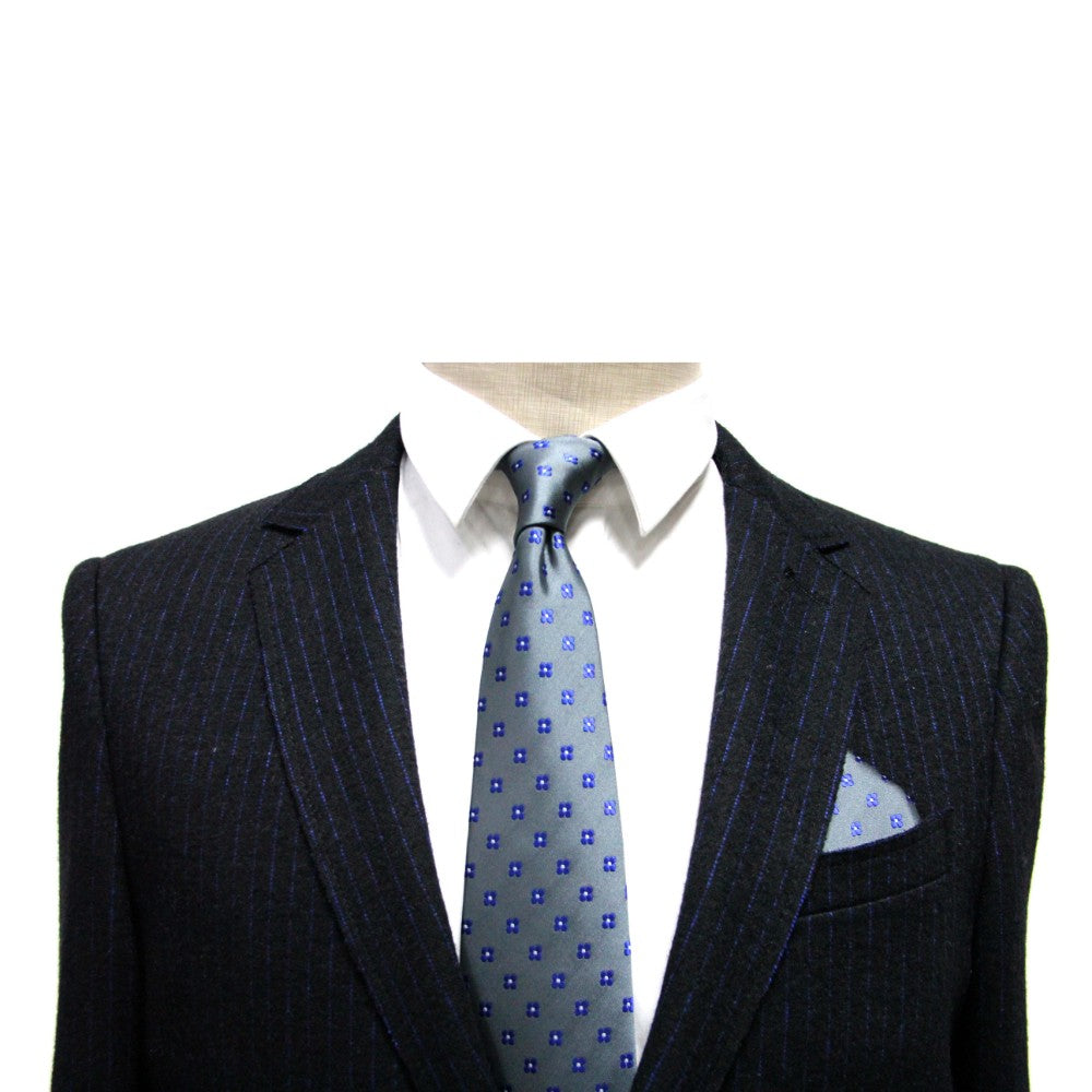 A stylish gentleman wears a pinstripe suit jacket with a white shirt and blue patterned tie. A Grey Blue Flower Pocket Square adds an elegant touch, neatly tucked into the breast pocket.