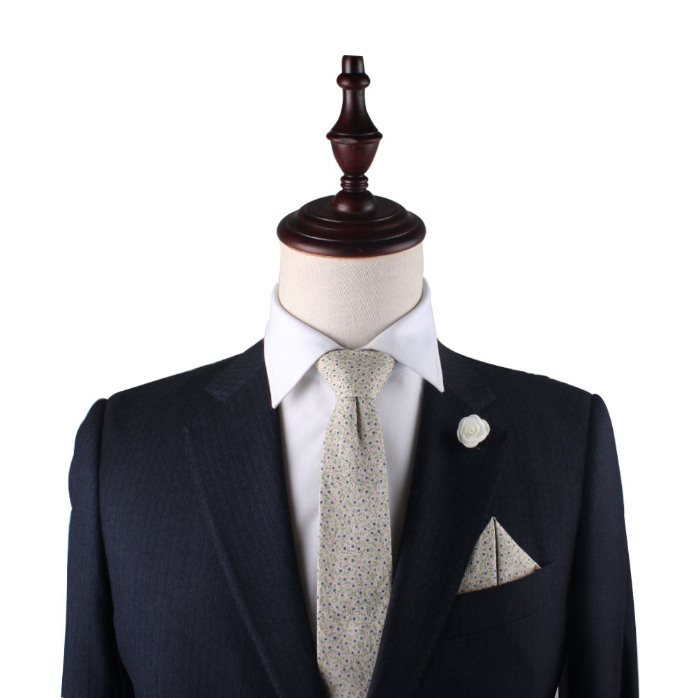 A dark suit on a mannequin exudes navy elegance with a white shirt, patterned tie, Blue Forget-Me-Nots Floral Pocket Square, and lapel pin, creating a statement of class.