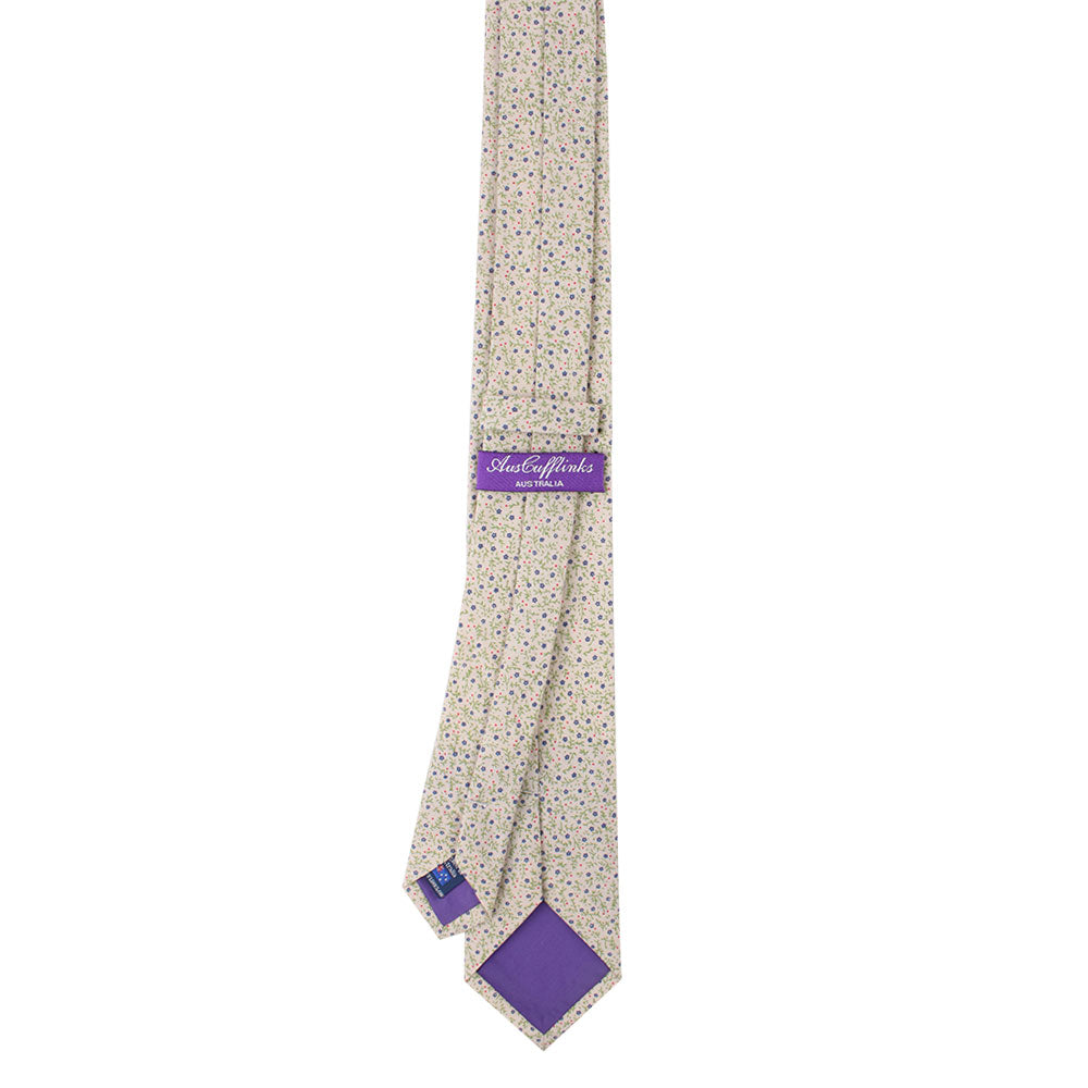The Blue Forget-Me-Nots Floral Skinny Cotton Tie exudes professionalism with its multicolored floral pattern, complemented by a purple label and purple lining on the back.