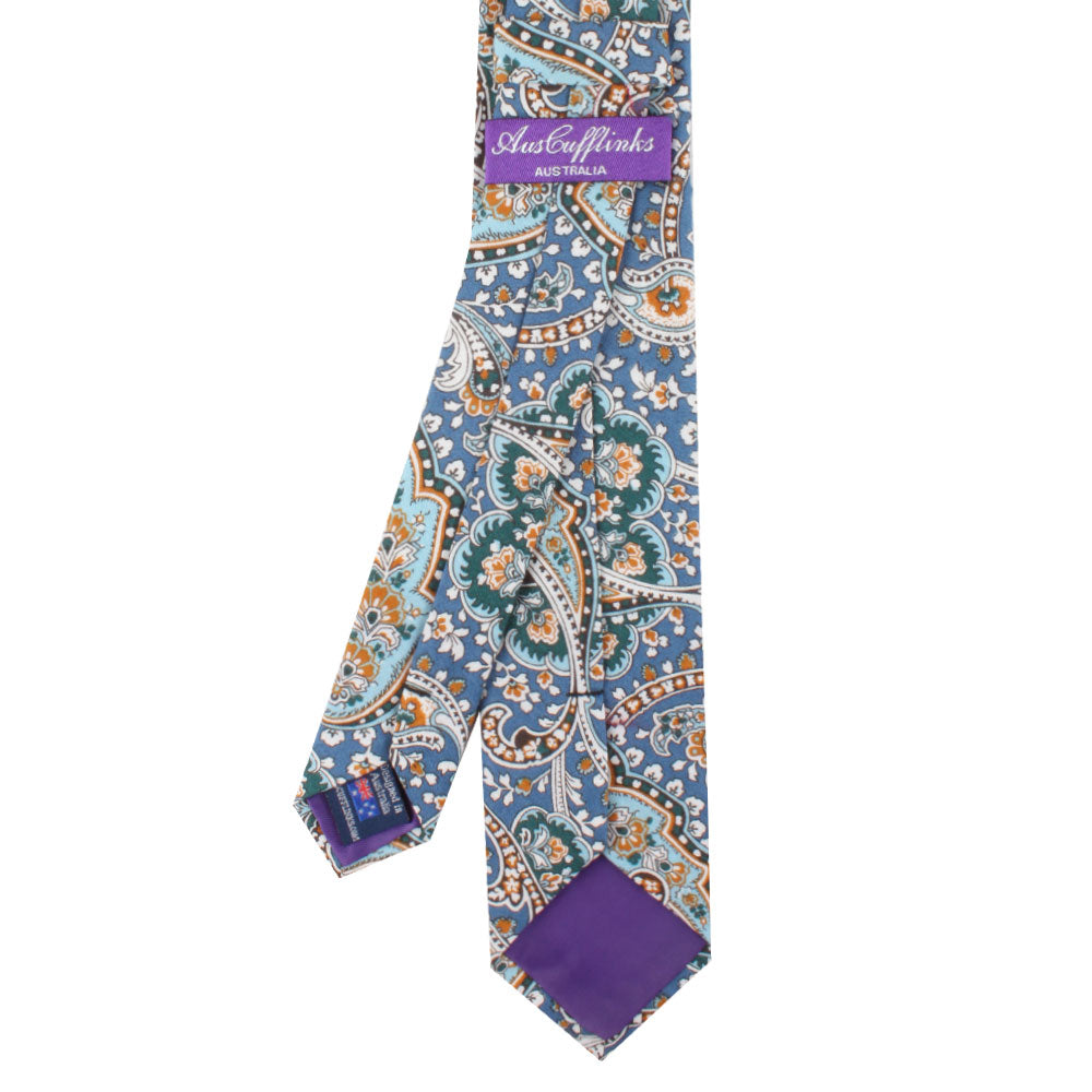 A necktie featuring a floral and paisley pattern with a blue, orange, and green design that subtly incorporates wave elements, labeled "Just Cufflinks Australia." This is the Blue Paisley Skinny Tie.