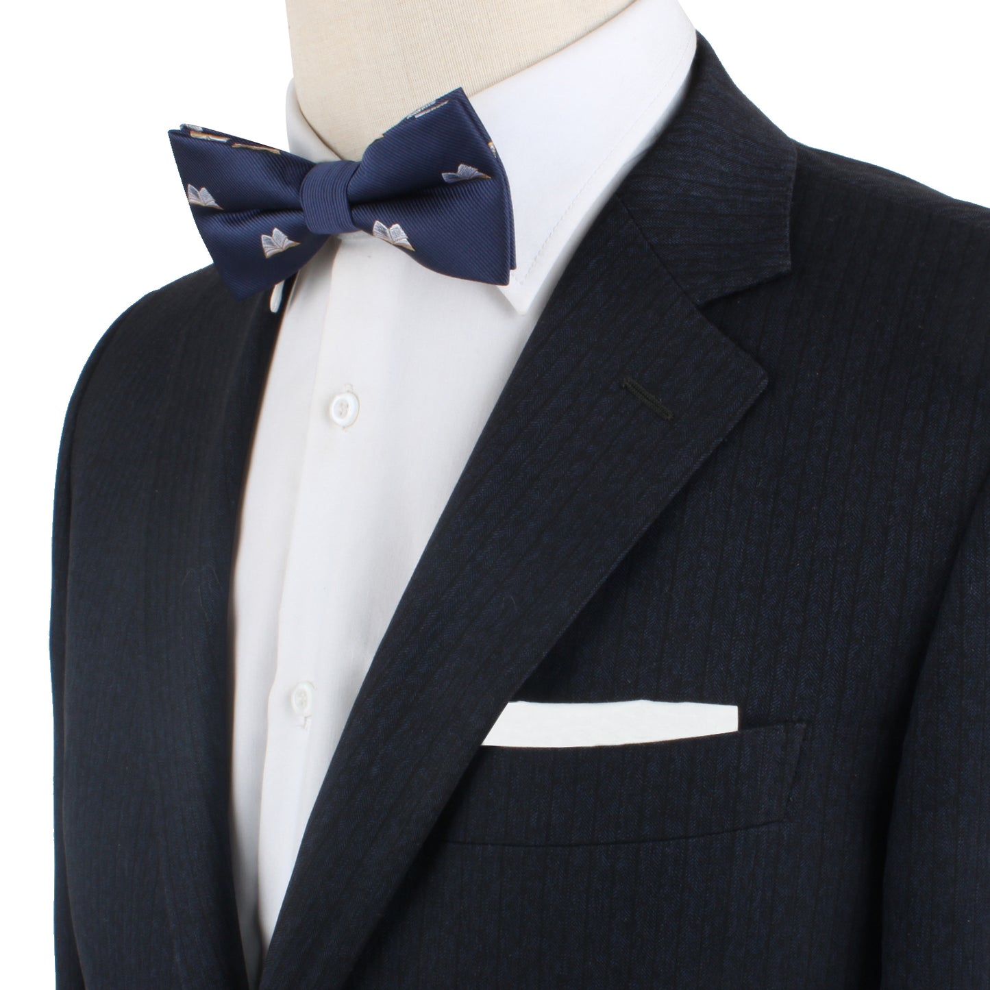 A person in a dark suit and white shirt, adorned with the sophisticated Book Bow Tie featuring delicate patterns and complemented by a crisp white pocket square—truly scripting their style to perfection.