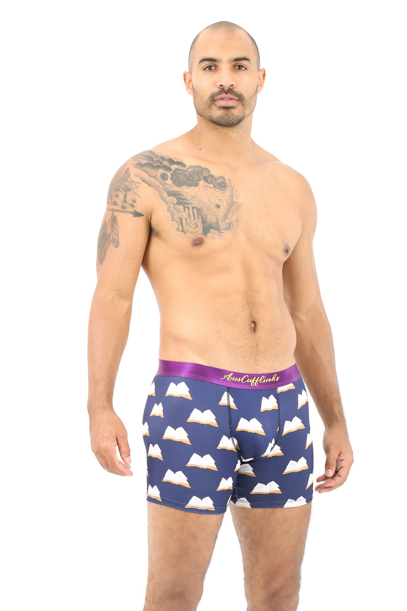A man with a shaved head and tattoo on his left shoulder wears Book Underwear – Fun Gift for Book Lovers, featuring navy blue boxer briefs with a mountain print and purple waistband, as he stands against a white background.