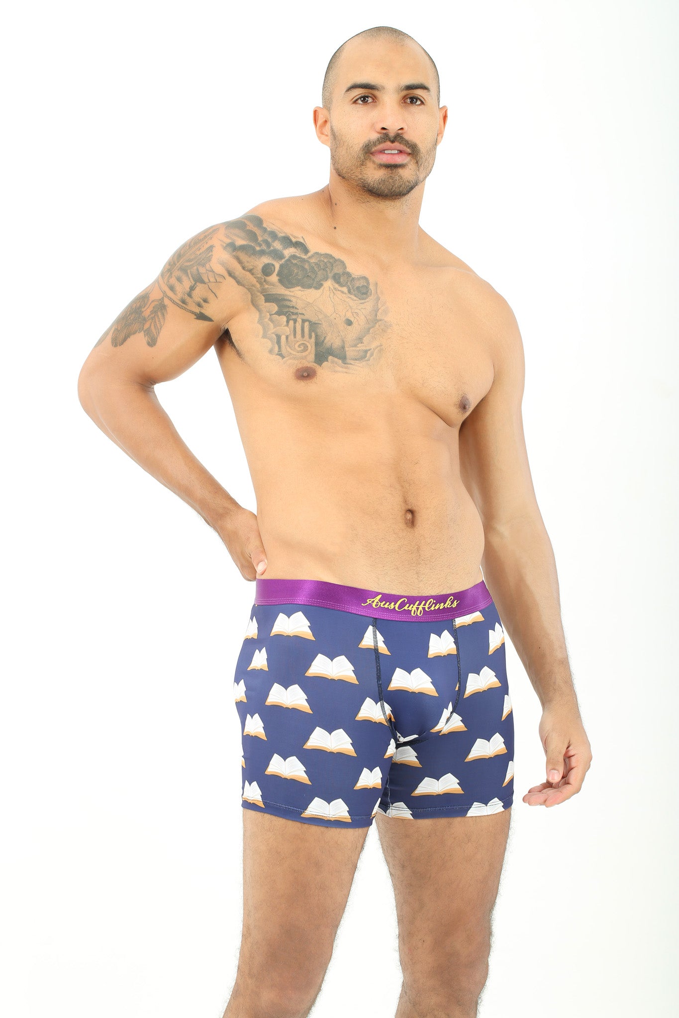 A man poses against a white background wearing Book Underwear – Fun Gift for Book Lovers in navy blue with a book print and purple waistband—ideal for those with literary passion.