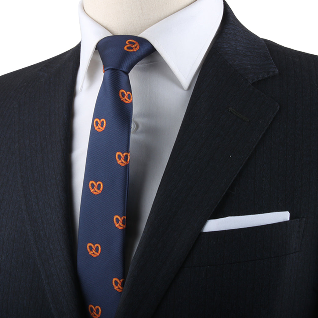 Close-up of a person in a dark pinstripe suit, wearing a white shirt and a Bagel Skinny Tie with orange pretzel patterns, exuding contemporary style, complete with a white pocket square in the suit's breast pocket.
