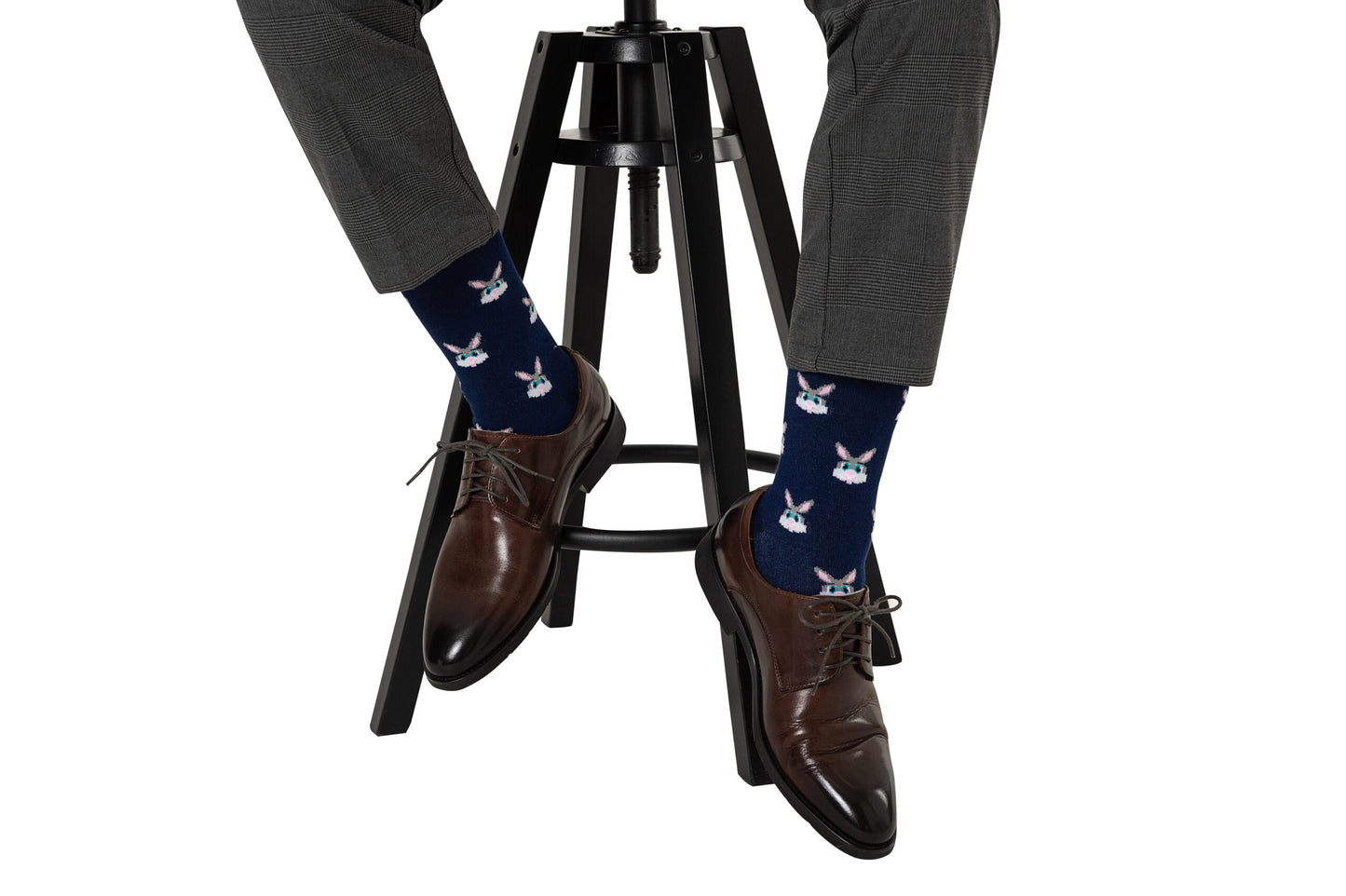 A person wearing brown shoes and blue socks with Bunny Socks on a stool.