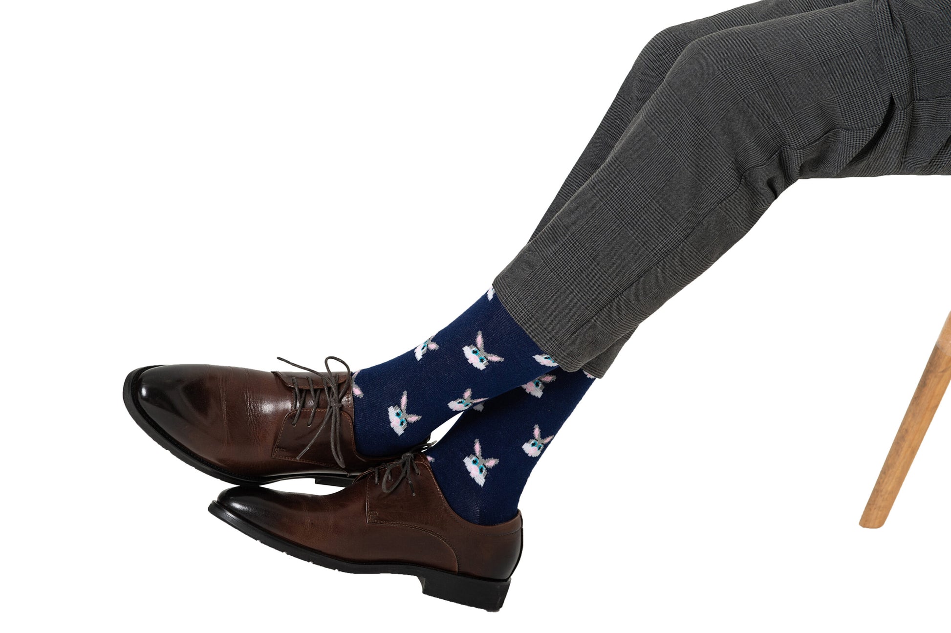 A pair of legs wearing brown shoes with blue socks and white Bunny Socks showcasing a playful collection of unique patterns.