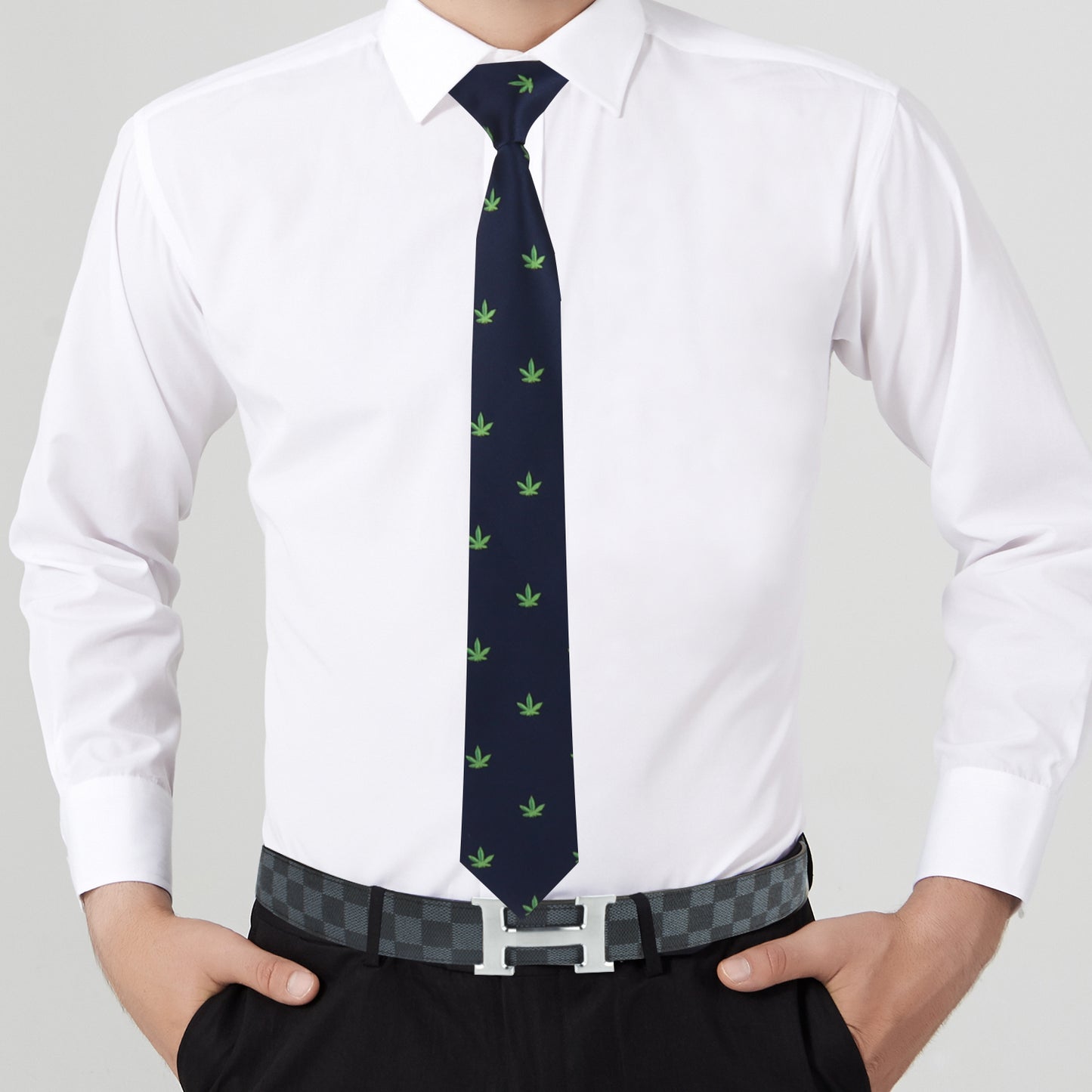 A man in a white shirt and black pants makes a bold statement with his Weed Skinny Tie featuring green leaf patterns and pairs it with a laid-back checkered belt.