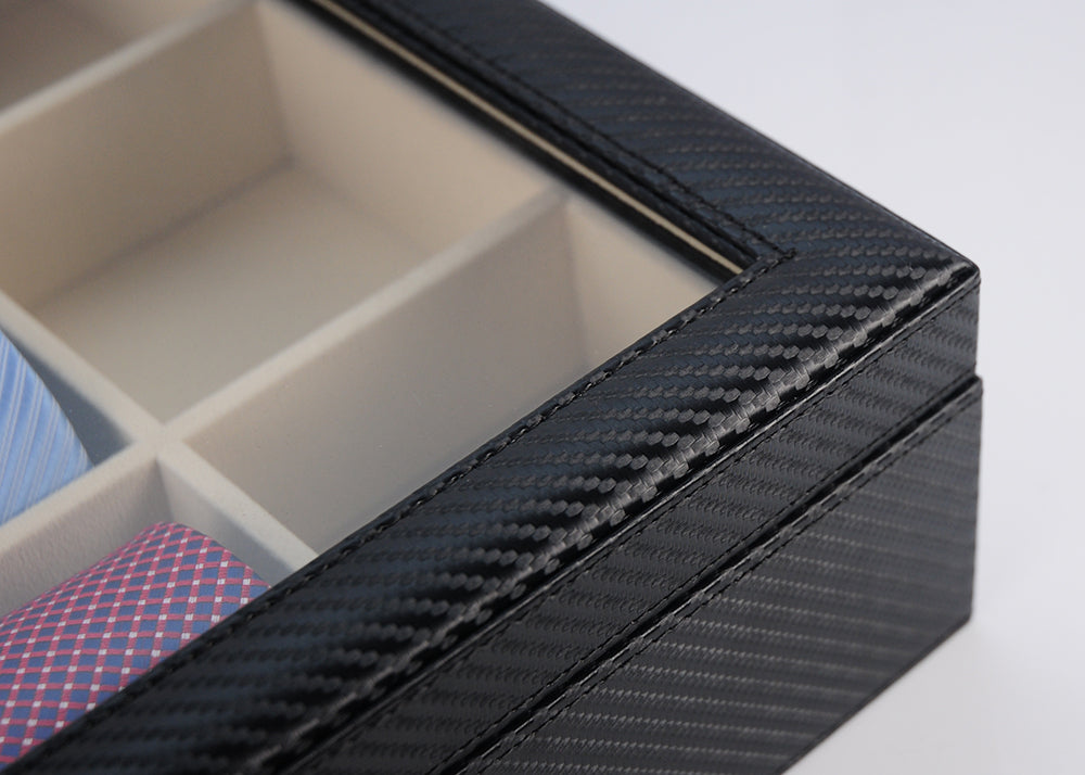 Close-up of the Carbon Fibre Tie Box, showcasing its black carbon fibre-patterned exterior, glass top, and beige compartments that neatly organize folded fabric items.