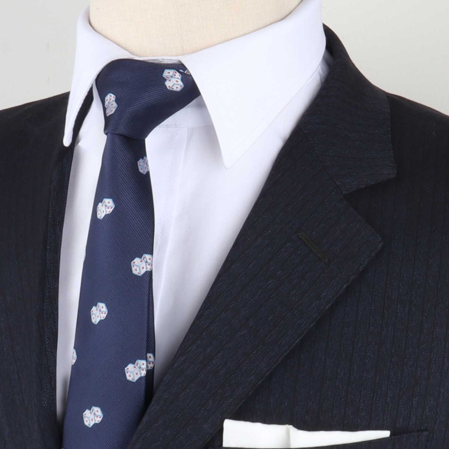 Close-up of a mannequin dressed in a dark pinstripe suit with a white shirt and the Casino Tie, featuring a navy color with a white pattern, complemented by a white pocket square. This ensemble captures the essence of timeless style with just a touch of luck.