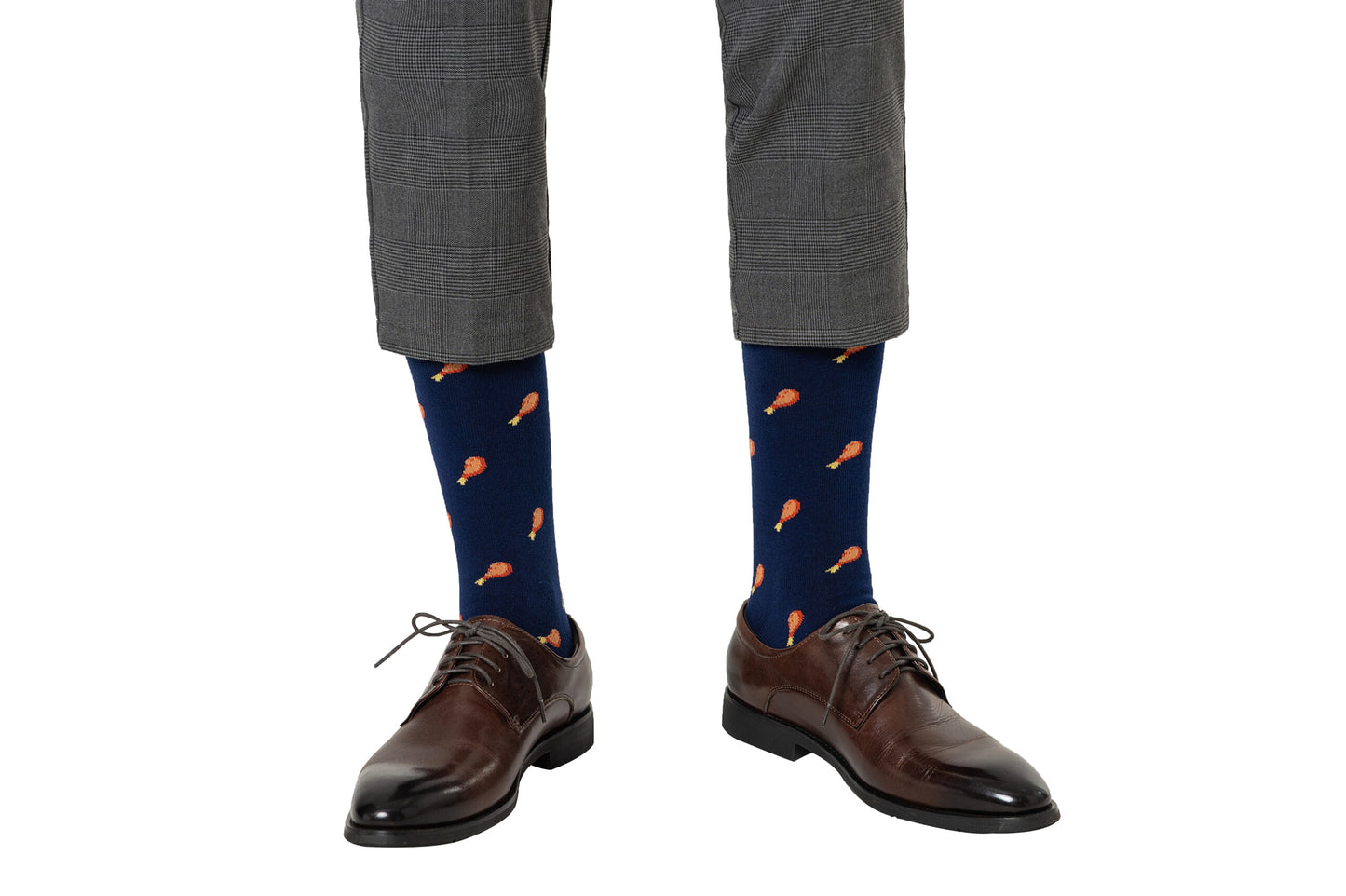 A person exhibiting a layered style is wearing gray plaid pants, brown dress shoes, and orange-patterned Strawberry Cake Socks.
