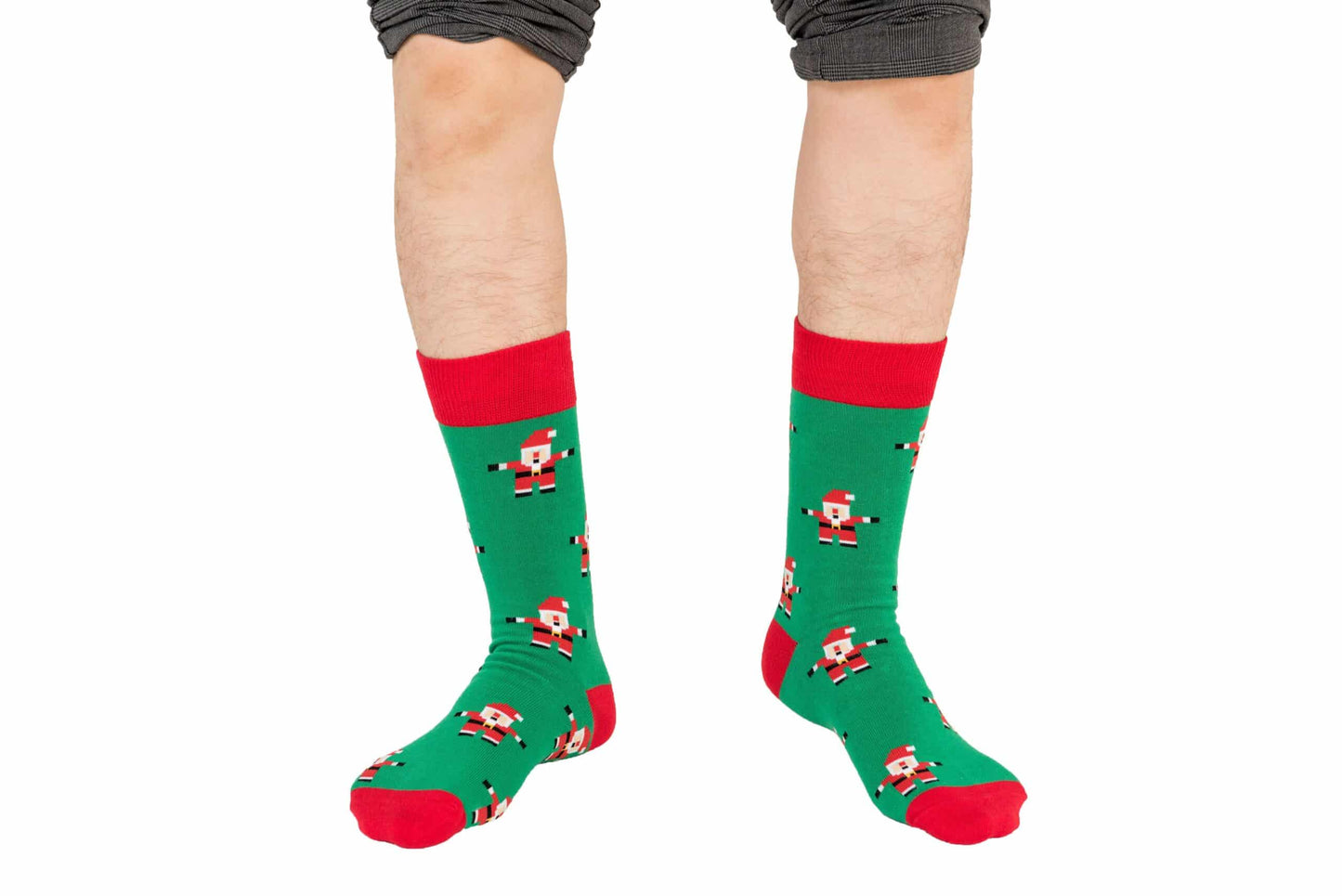 Someone wearing Santa Socks, which feature a festive green with red trim and a cheerful Santa Claus design, radiating holiday spirit. The lower legs are visible, with the pants rolled up above the merry feet.
