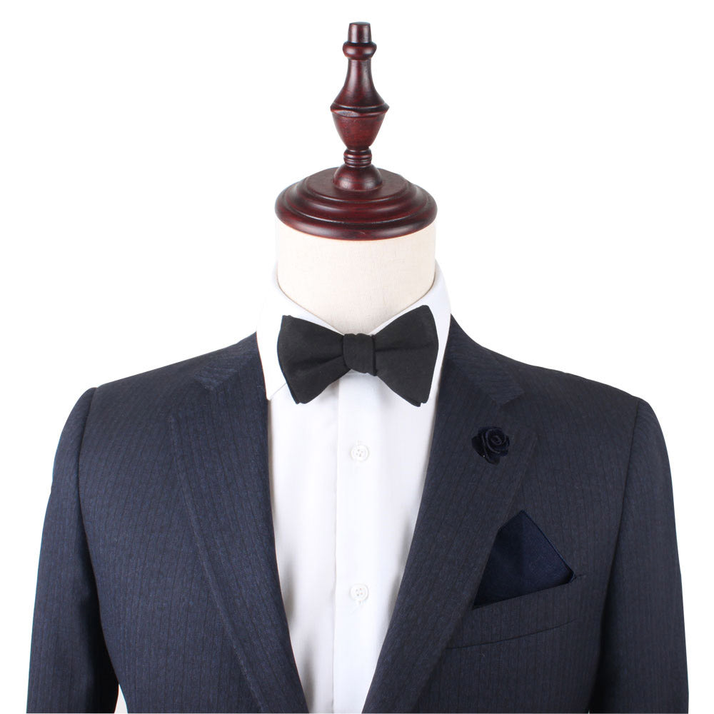 Mannequin dressed in a dark pinstripe suit featuring a white shirt, the Classic Cotton Black Self Tie Bow Tie, and a black pocket square. A decorative lapel flower adorns the left side, ideal for formal events.