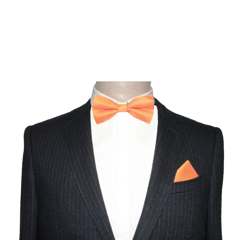 A mannequin dressed in a dark pinstripe suit exudes elegance with a crisp white shirt, while making a bold statement with the Classic Orange Bow Tie and matching pocket square.