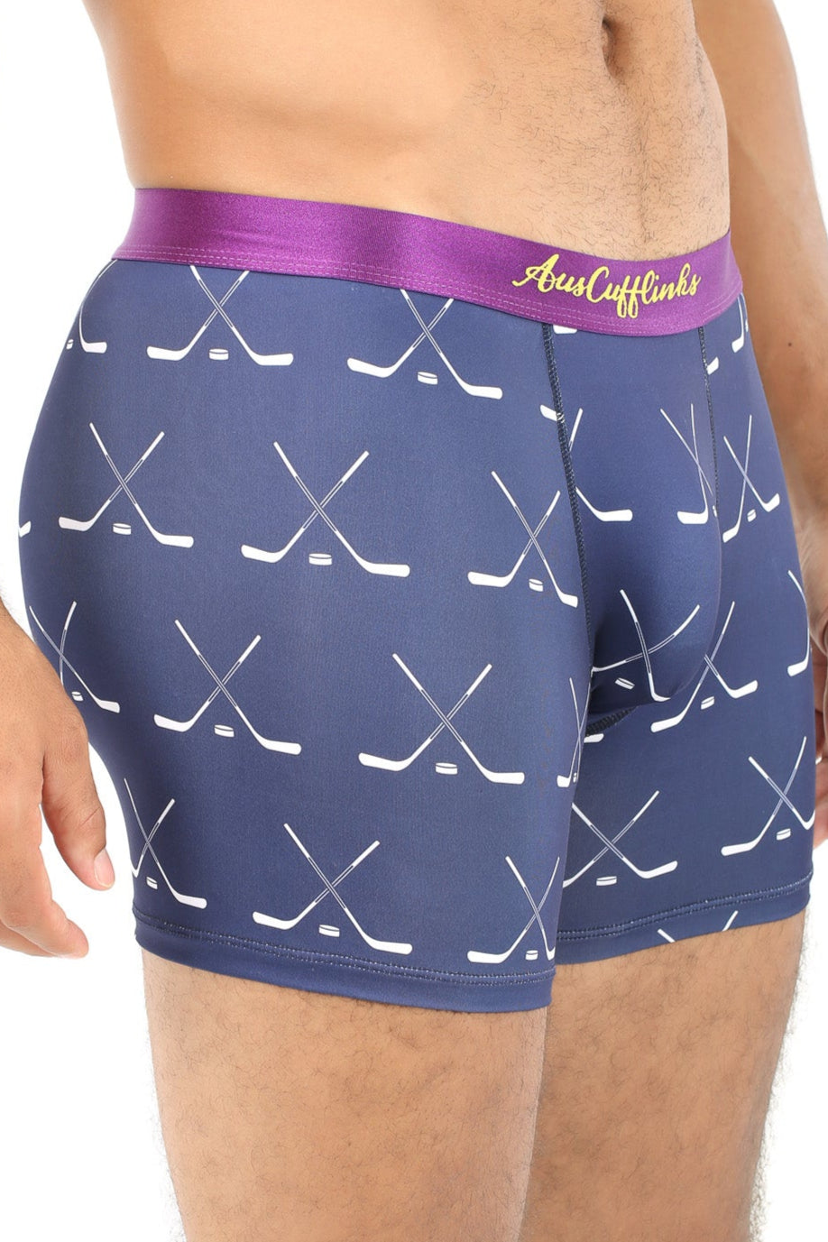 A man wearing the Crossed Ice Hockey Underwear, which features a stylish navy dual stick hockey pattern and a purple waistband, stands in a side pose to highlight both comfort and fashion.