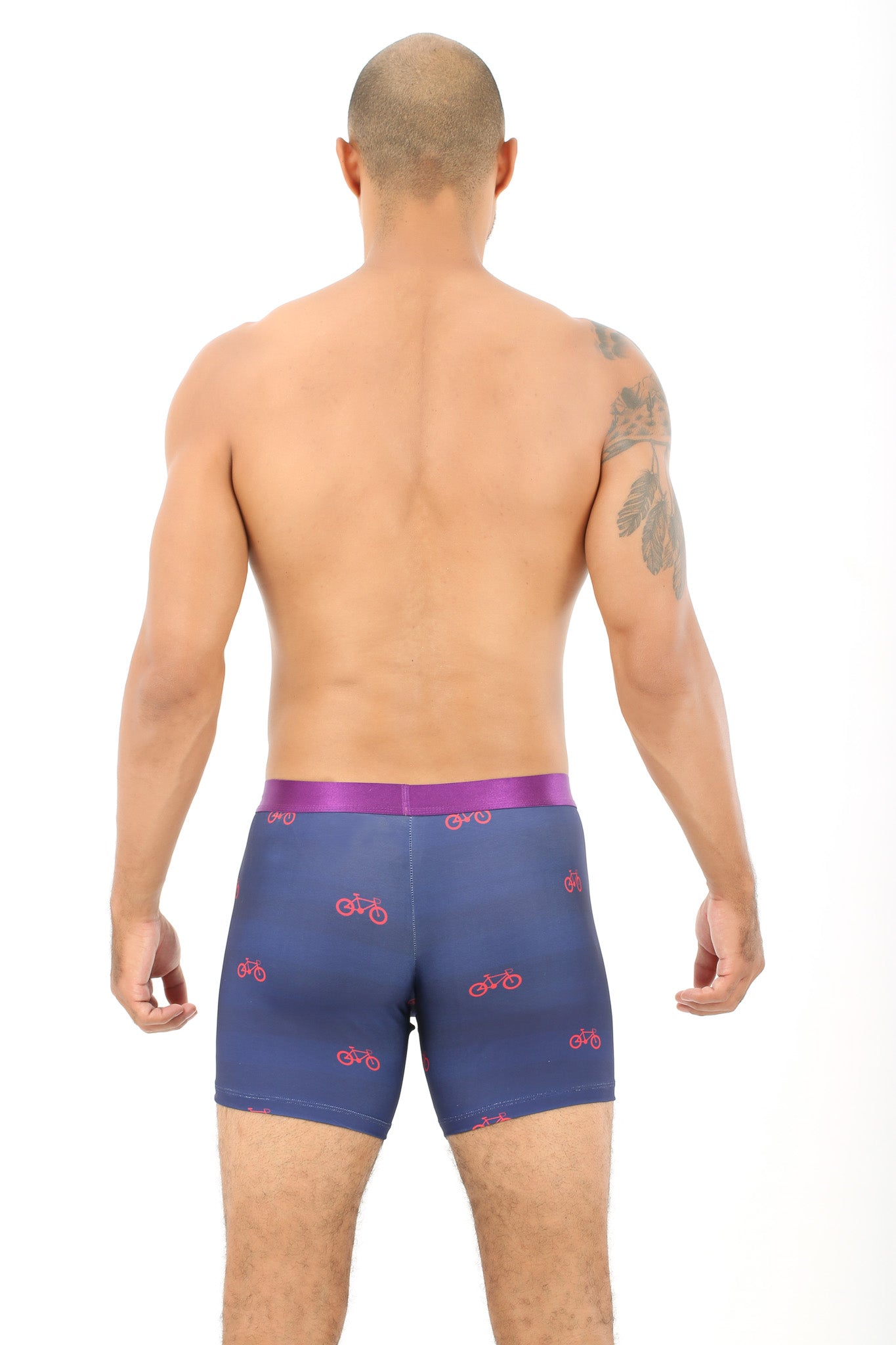 A man faces away from the camera, wearing Cyclist Underwear – Fun Gift for Riders: blue boxer briefs with red bicycle prints and a purple waistband, ideal for cycling fans, set against a plain white background.