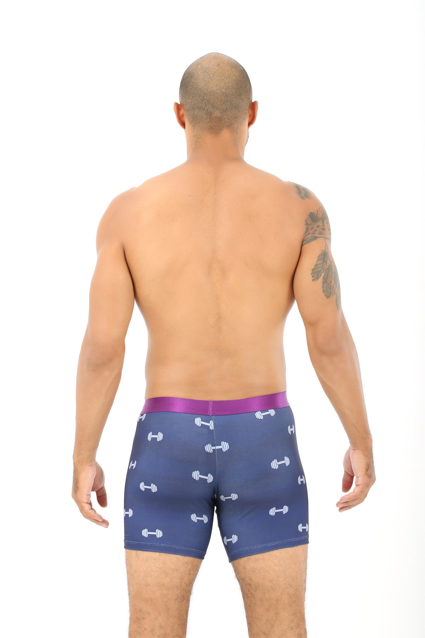 A person with a tattoo on their shoulder is seen from behind, wearing Gym Underwear in purple and blue featuring a dumbbell pattern, embodying the spirit of the lift game, against a white background.