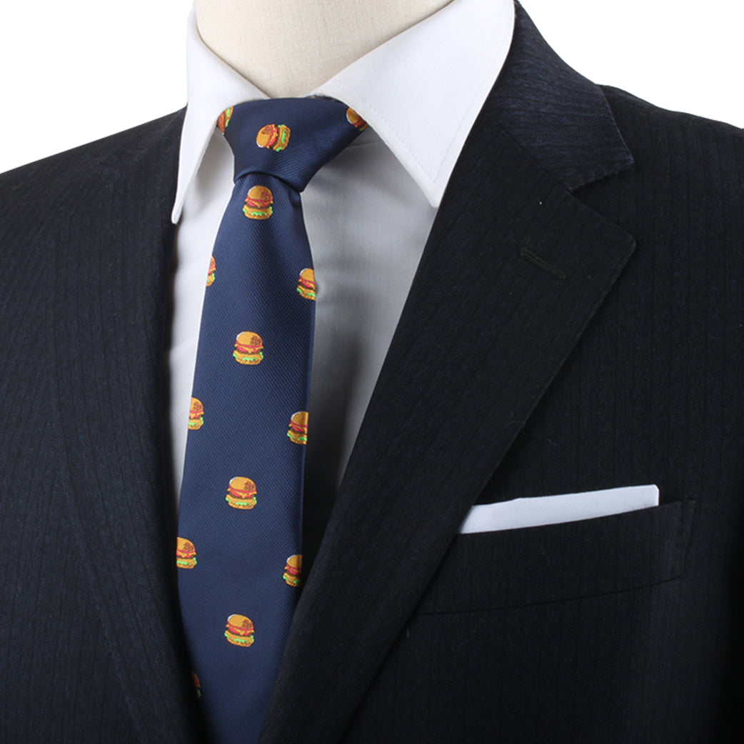 A person in a dark suit with a white shirt is making a bold style statement wearing the Burger Skinny Tie, featuring small, universally adored hamburger images.
