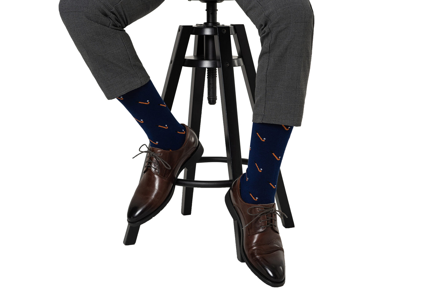 A person wearing gray plaid pants, brown dress shoes, and Field Hockey Socks sits on a black stool against a white background.