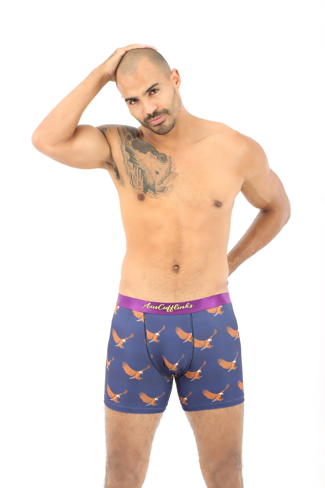A man with short hair poses comfortably in a pair of Flying Eagle Boxer boxer briefs, featuring a patterned design, as he stands against a white background and touches the top of his head.