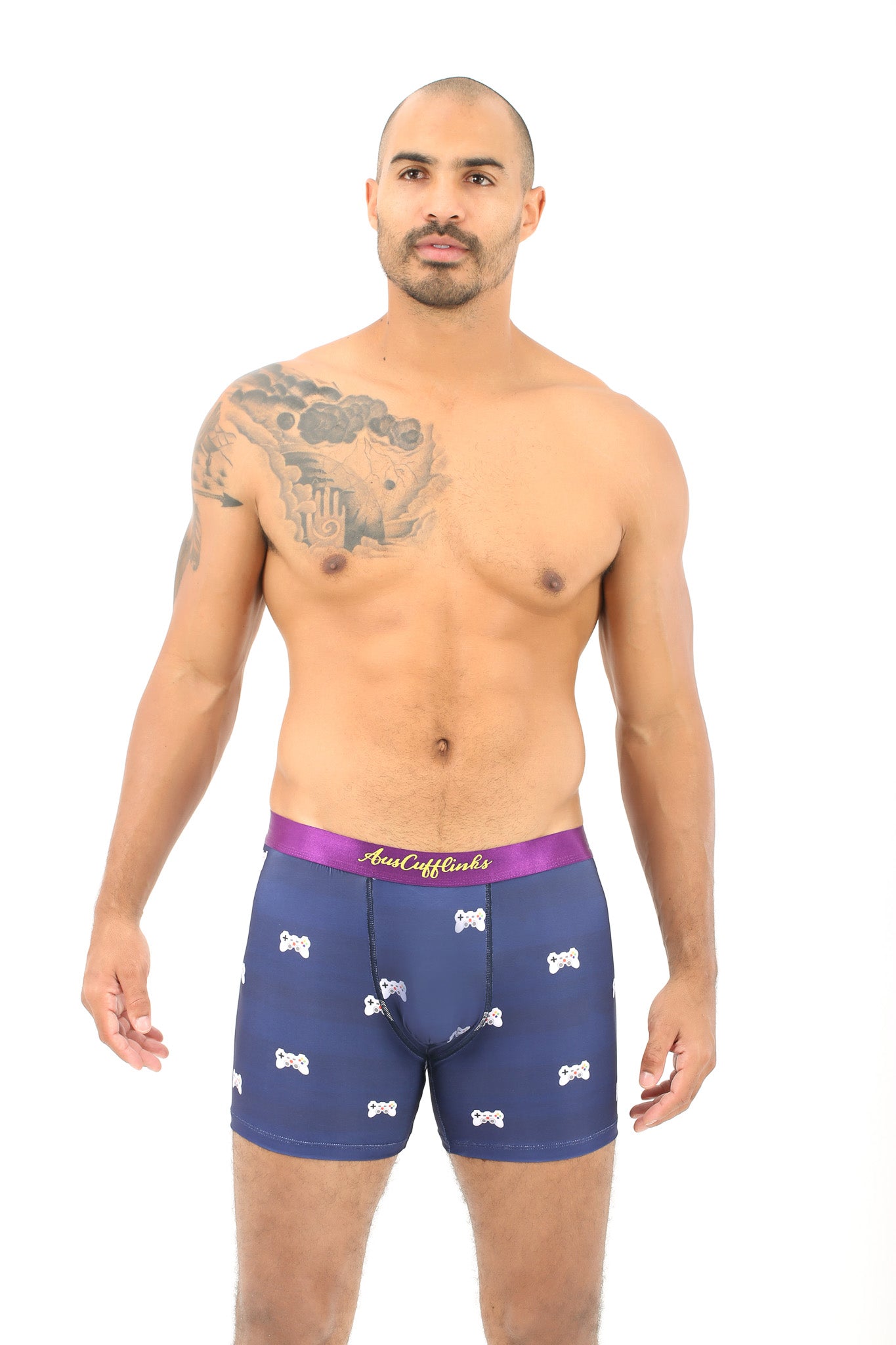 A man with a tattoo on his shoulder is reveling in peak comfort wearing the Game Controller Boxer, featuring a navy blue color with a patterned design and complemented by a stylish purple waistband, ready to elevate his style.