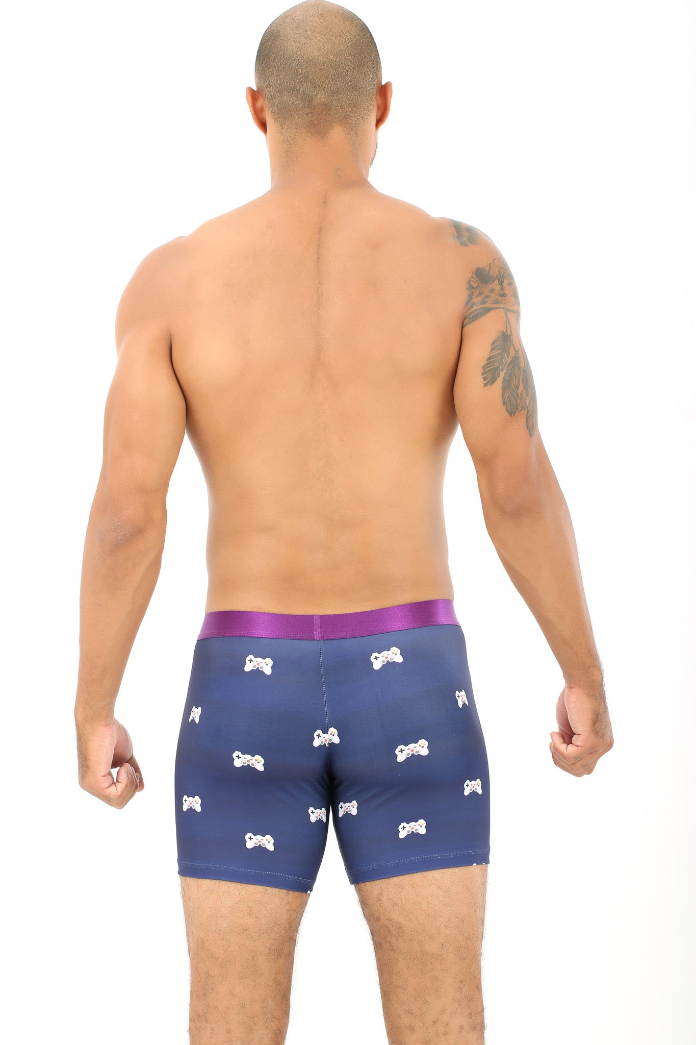 A person with a tattoo on their arm stands facing backward, wearing the Gamer Underwear, adorned in blue with a white pattern, embracing the comfort needed to level up in their personal game.