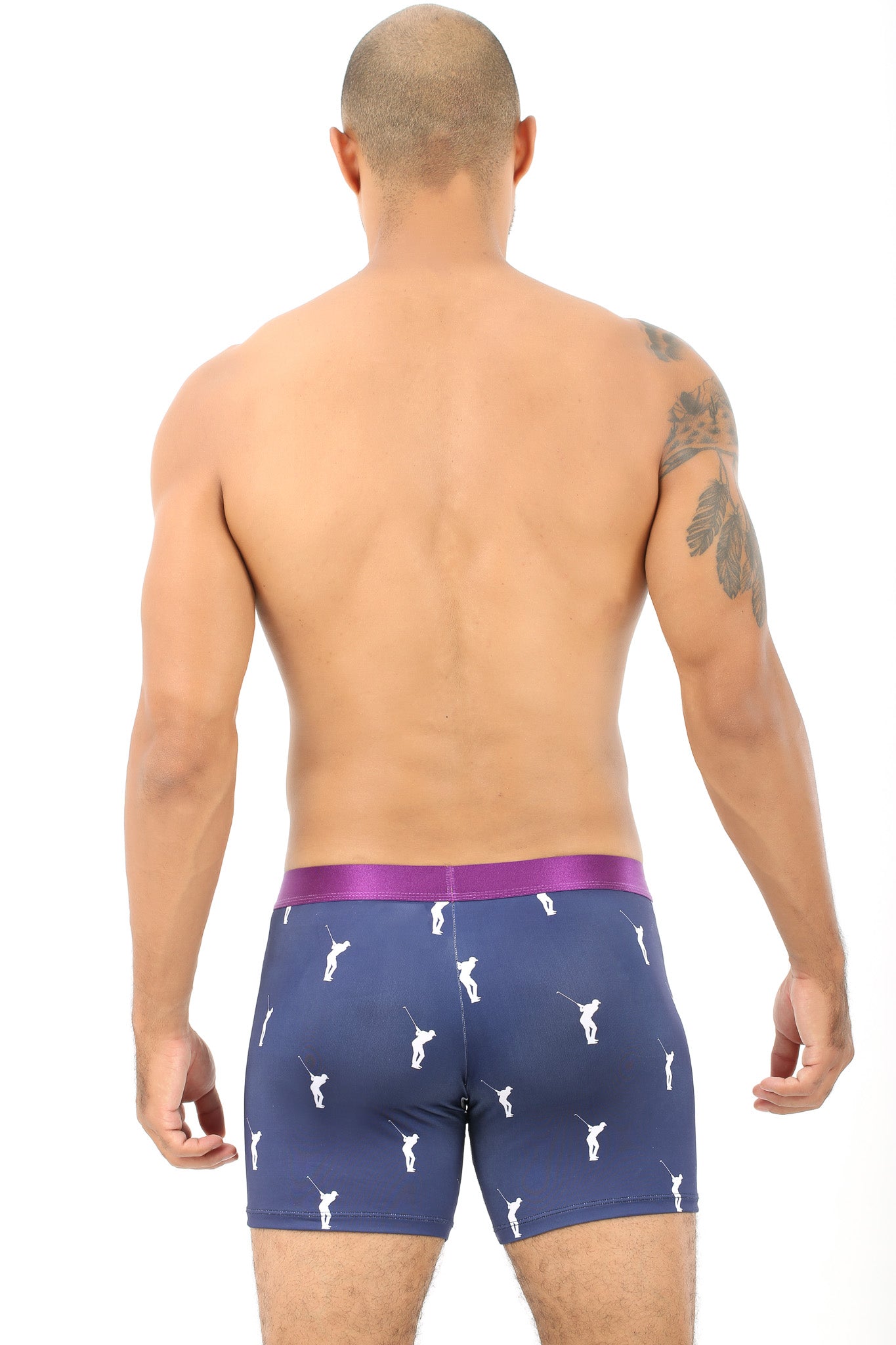 A shirtless man is shown from the back, wearing Golf Swing Print Underwear in dark blue with a pattern of small white figures. He has a tattoo on his left arm, exuding an effortless air of comfort.