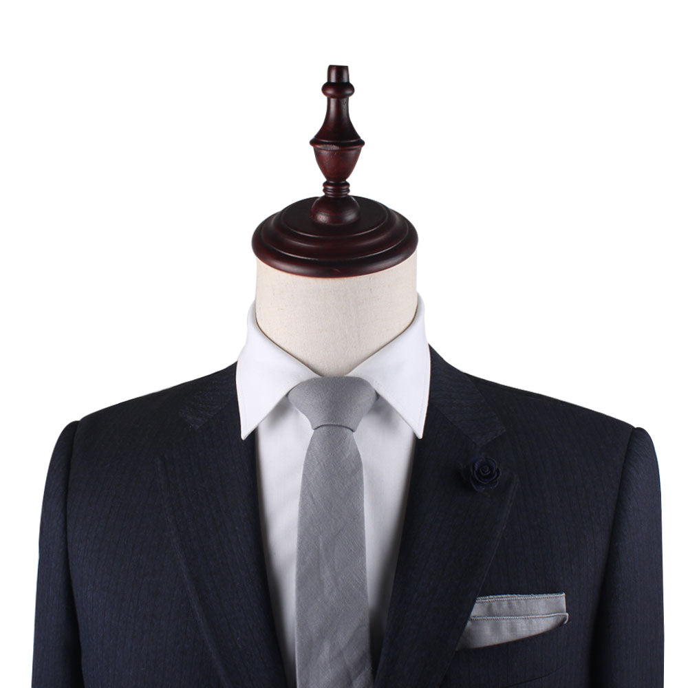 A mannequin in a dark suit is styled with a white shirt and the Grey Cotton Business Tie & Pocket Square Set, ideal for groomsmen gifts, complemented by a decorative lapel pin.