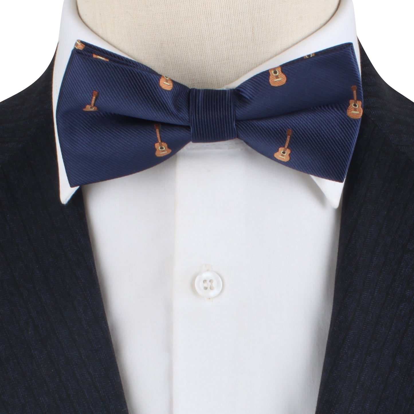 A close-up of a person wearing the Guitar Bow Tie, which is navy blue with small guitar prints, perfectly paired with a white dress shirt and a dark suit jacket, exuding impeccable style.