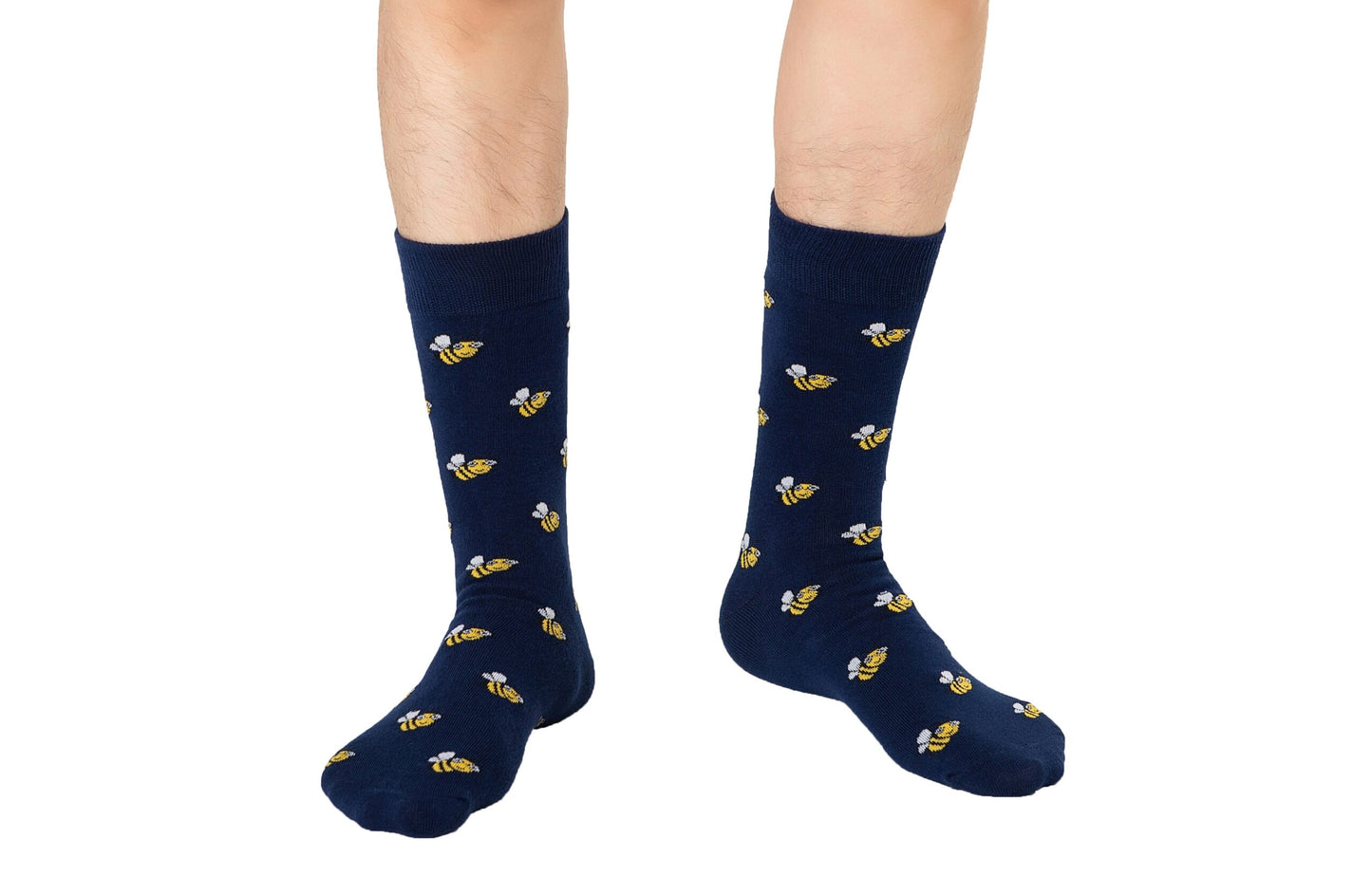 A person stands on a white background wearing Bee Socks—navy blue socks with a yellow bee print.