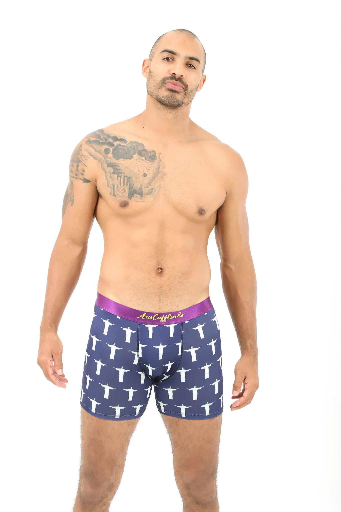 A man with a tattoo is standing in a pair of Jesus Underwear, featuring blue boxer briefs with white patterns, exuding a heavenly feel against the white background.