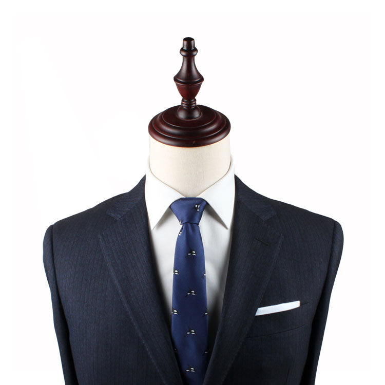A mannequin exudes contemporary elegance, adorned in a dark suit, white dress shirt, and Killer Whale Thin Tie, complete with a white pocket square.