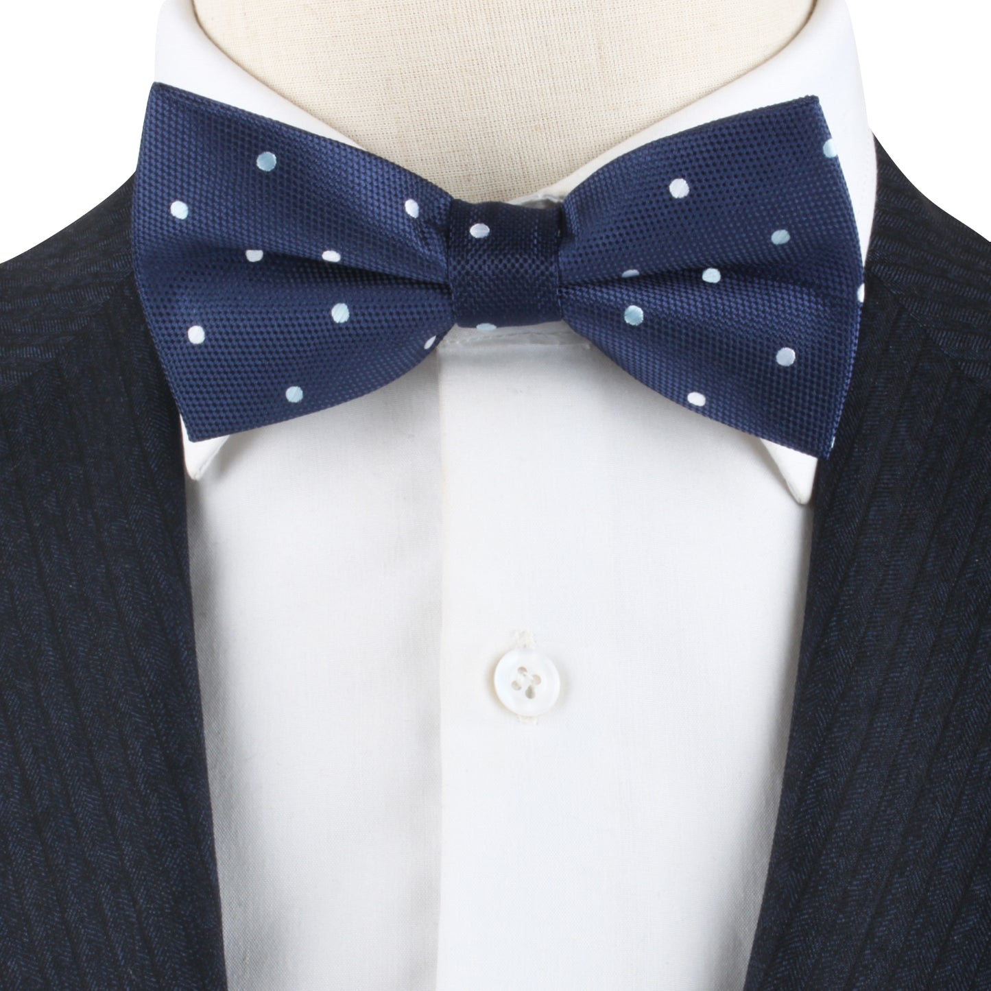 Close-up of a White and Blue Polka Dot Bow Tie elegantly paired with a crisp white dress shirt, beneath a sophisticated dark striped suit jacket.