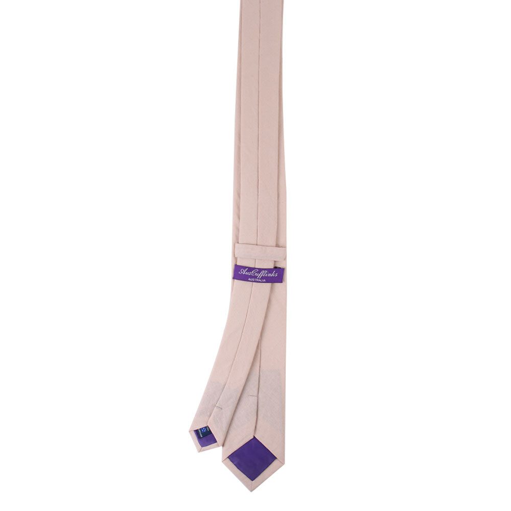 A cream pink skinny cotton tie with a soft touch features a purple label and tip detail, laid flat.