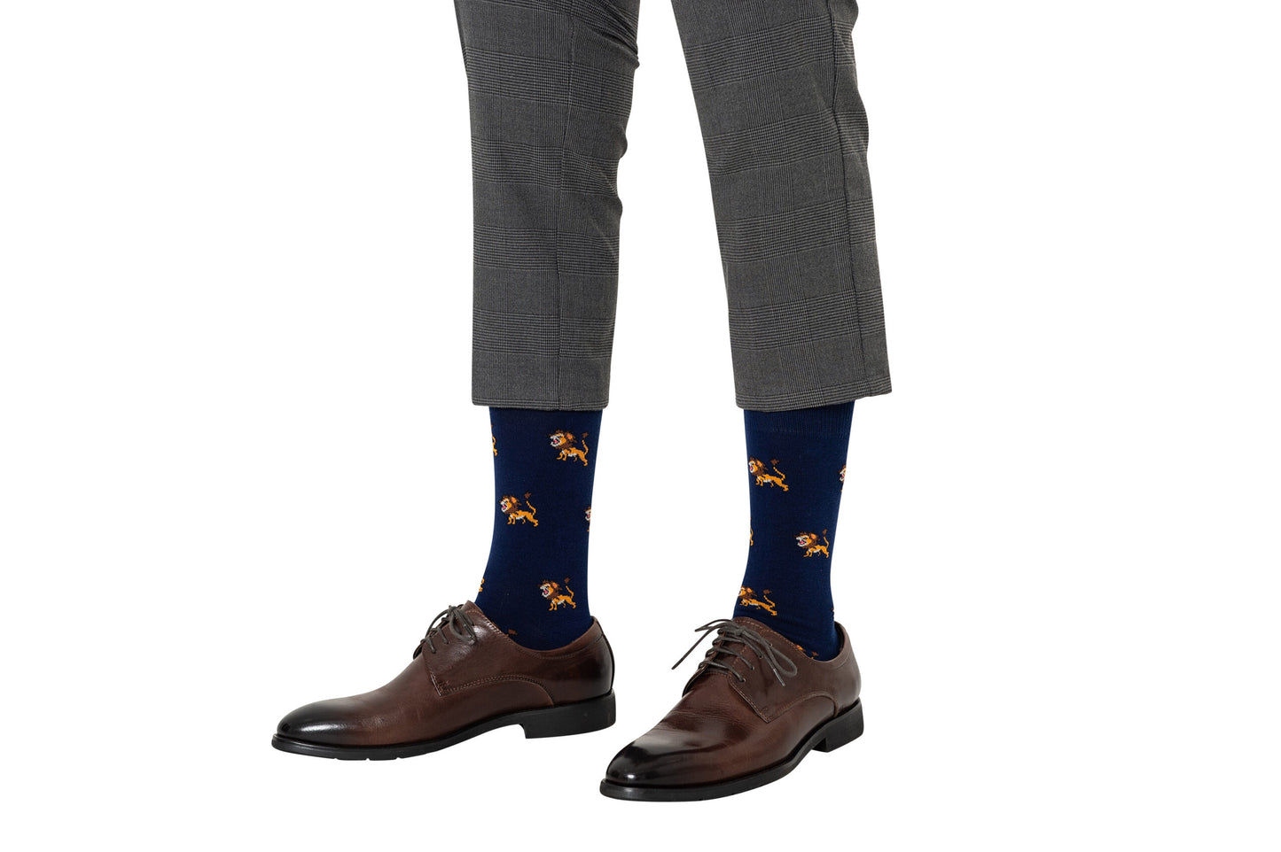 A person wearing gray checkered pants, brown leather dress shoes, and navy blue Lion Socks with orange lion patterns.